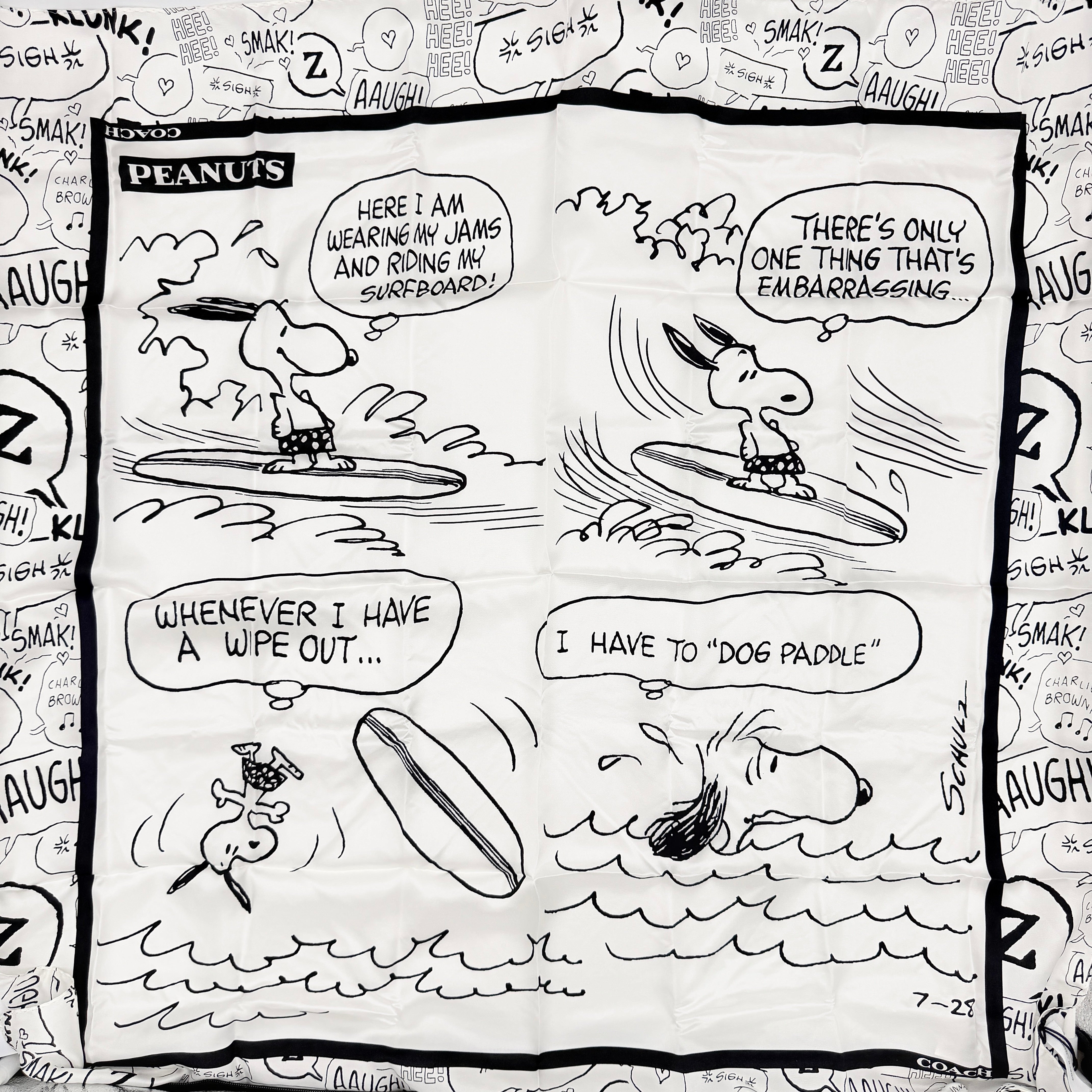 Coach x Peanuts black and white silk scarf featuring a Snoopy surfing comic print, shown with Coach packaging and tags.