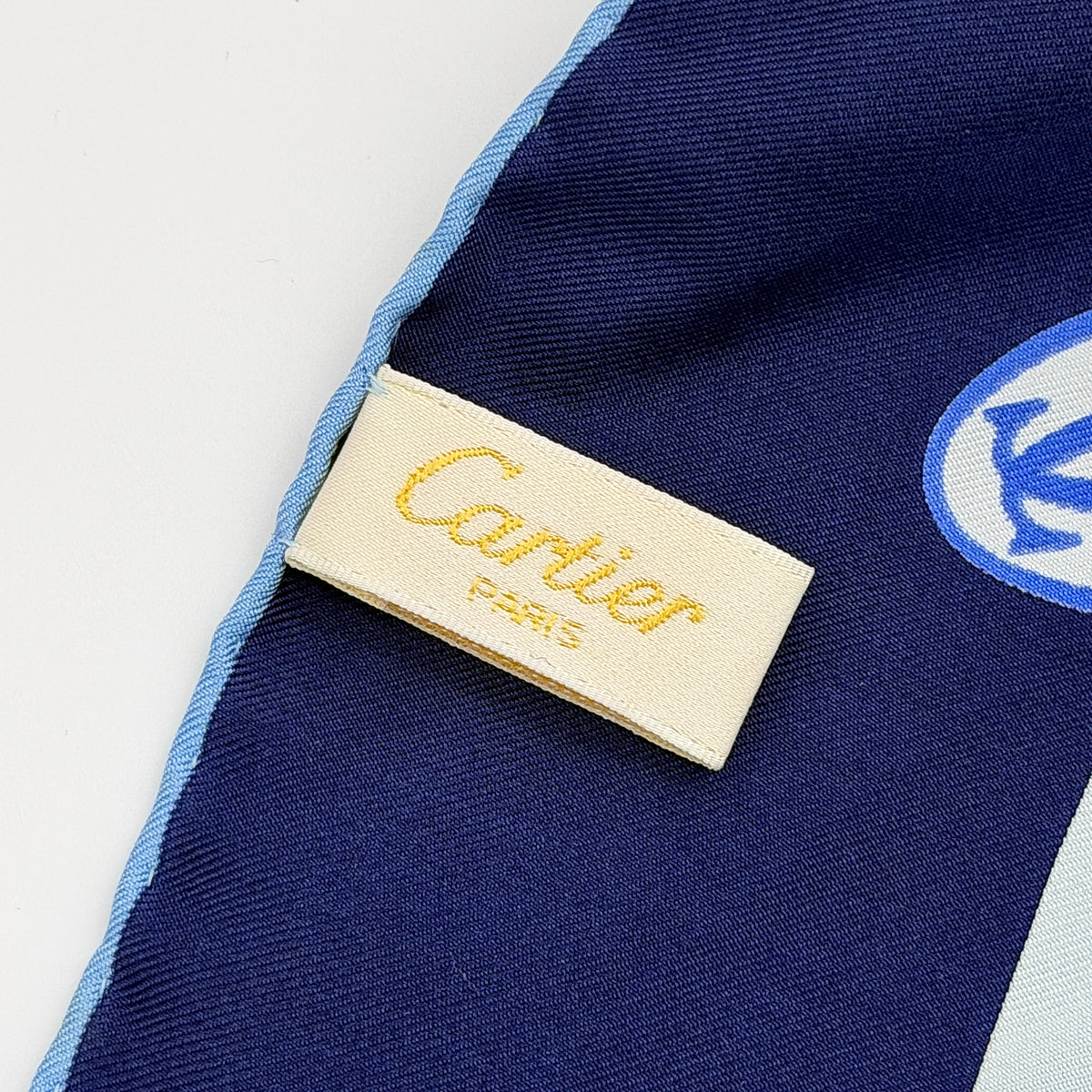 Cartier silk scarf in blue and white with graphic monogram logo print and navy border, elegantly arranged.