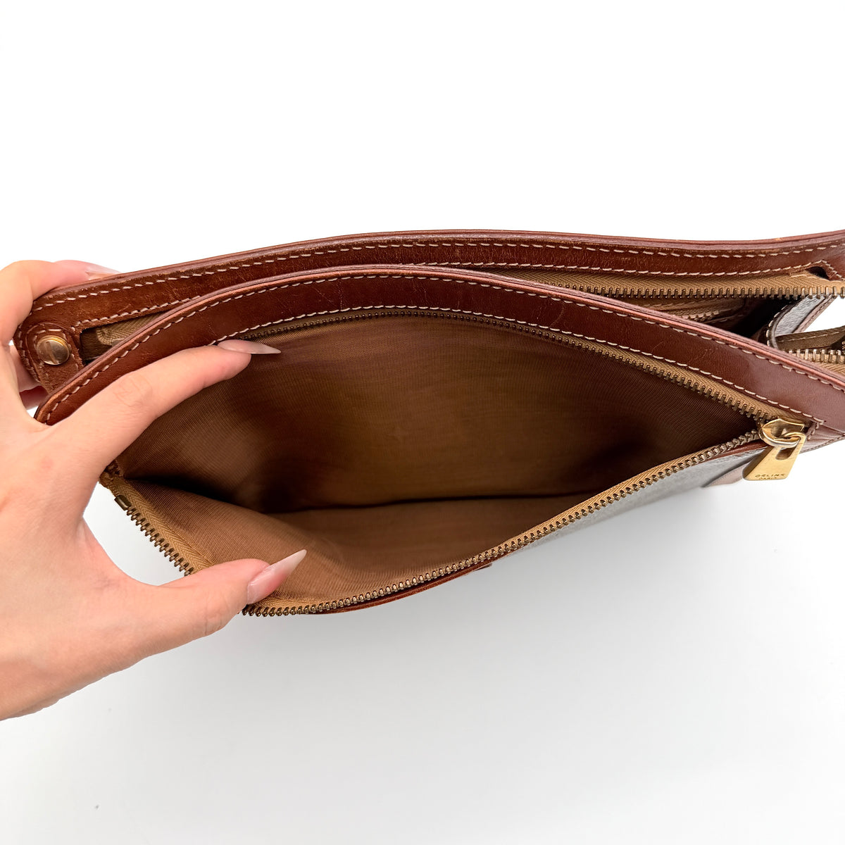 Celine Triomphe Macadam clutch bag in brown canvas with tan leather trim and gold hardware, shown with wrist strap.