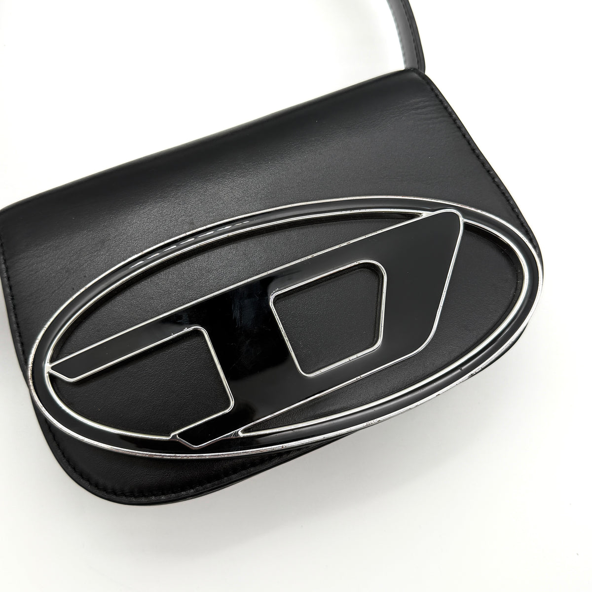 Diesel 1DR Shoulder Bag in black leather with a bold silver and black D logo plaque on the front flap.