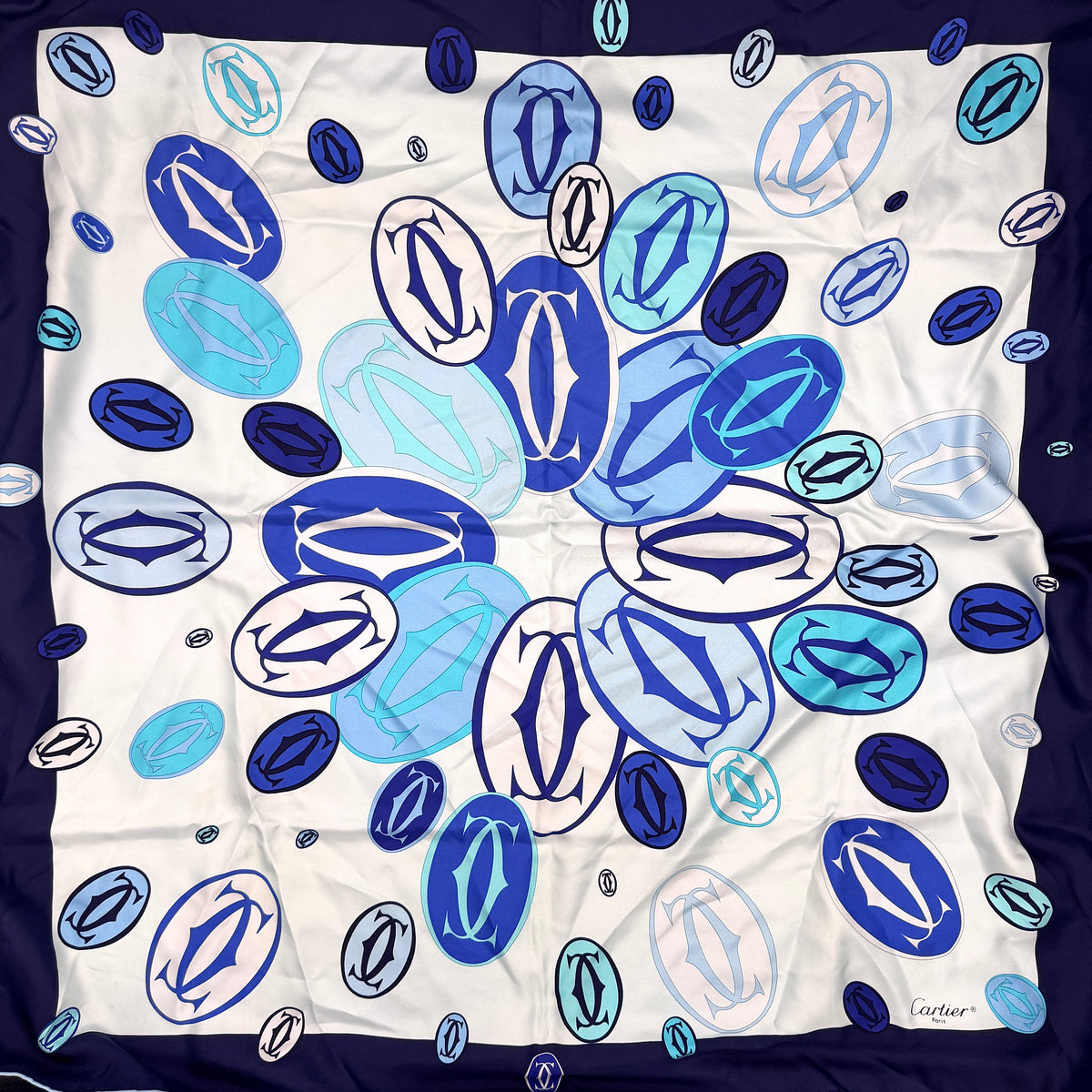 Cartier silk scarf in blue and white with graphic monogram logo print and navy border, elegantly arranged.