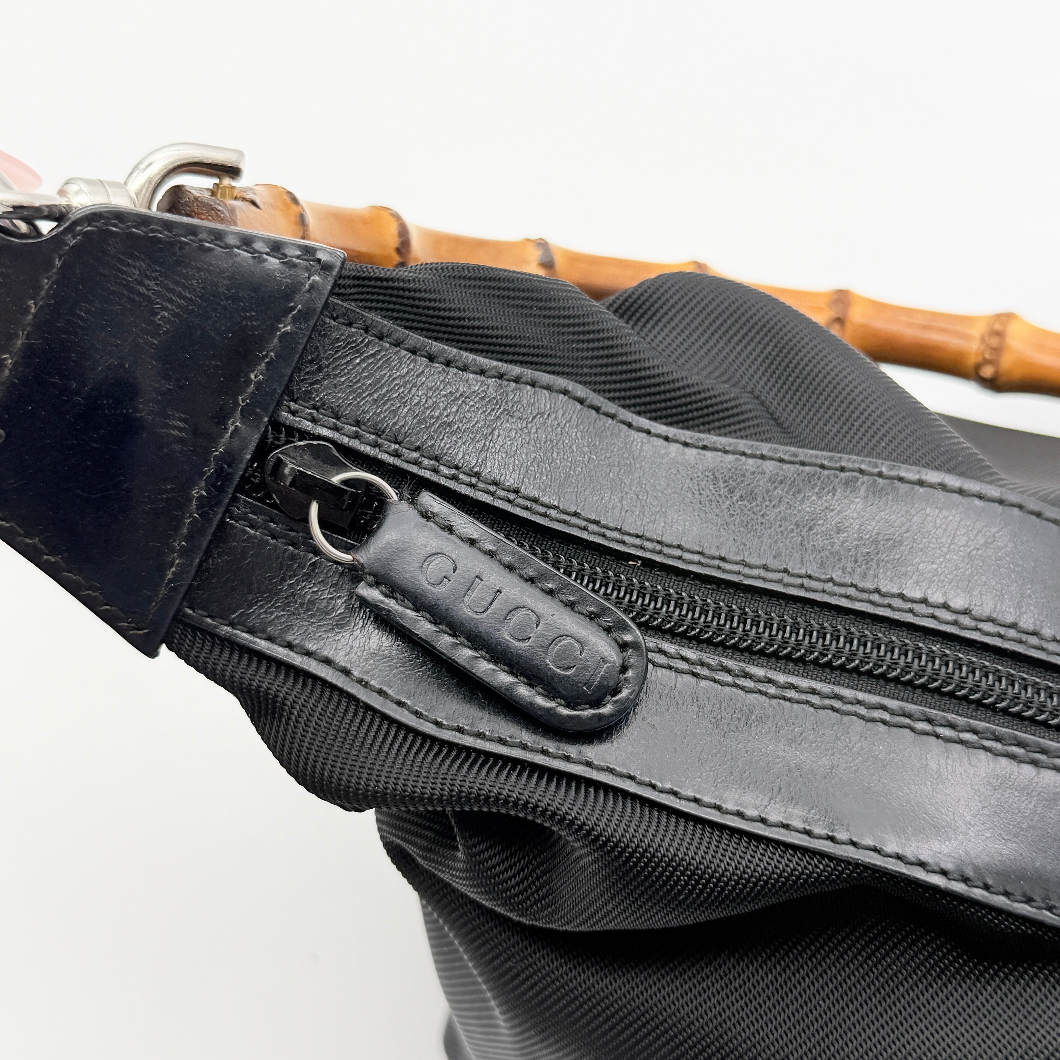 Gucci black nylon shoulder bag with bamboo handle and leather trim, photographed against a white background.