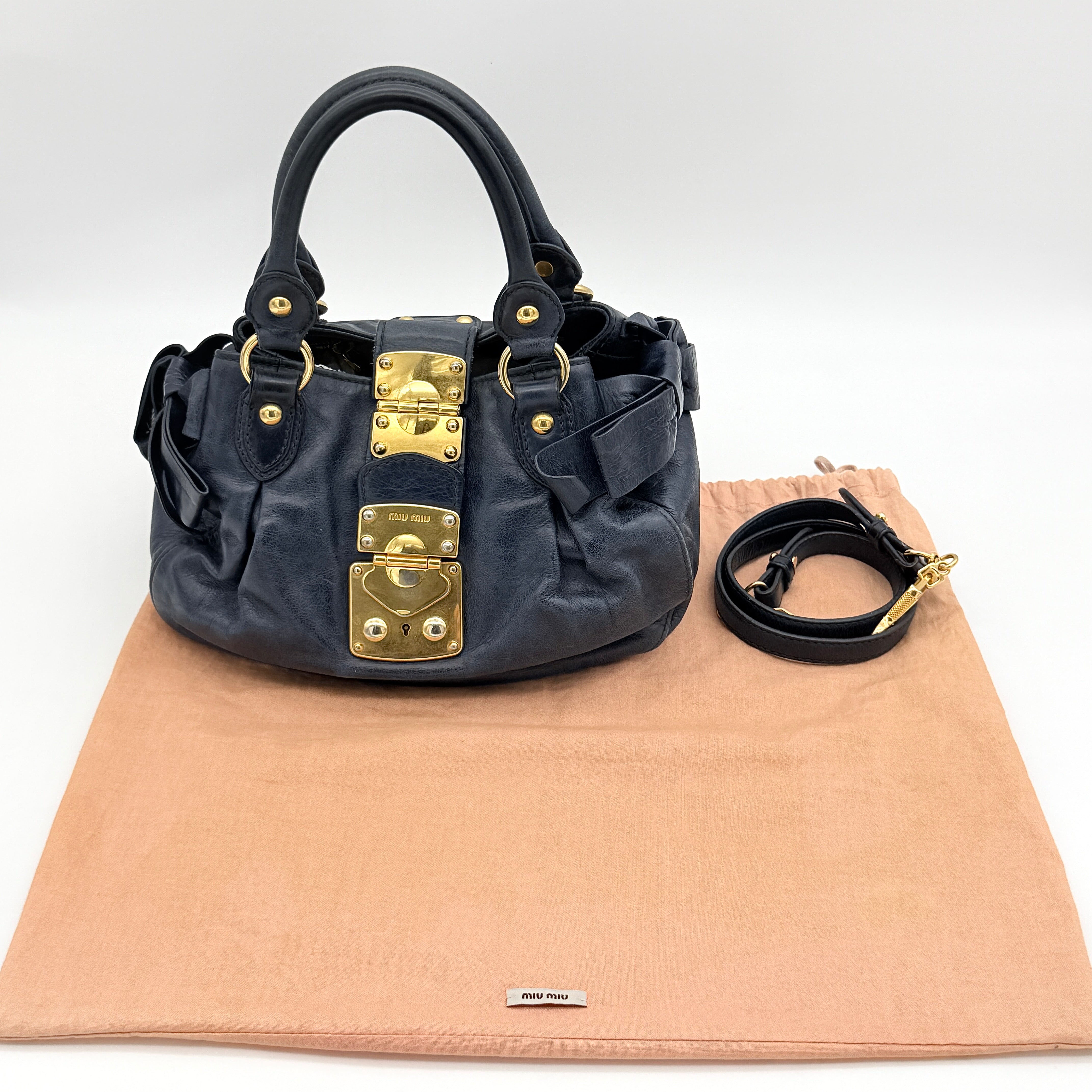 Miu Miu navy blue Vitello Lux Bow Satchel with gold-tone hardware, detachable strap, and dust bag.