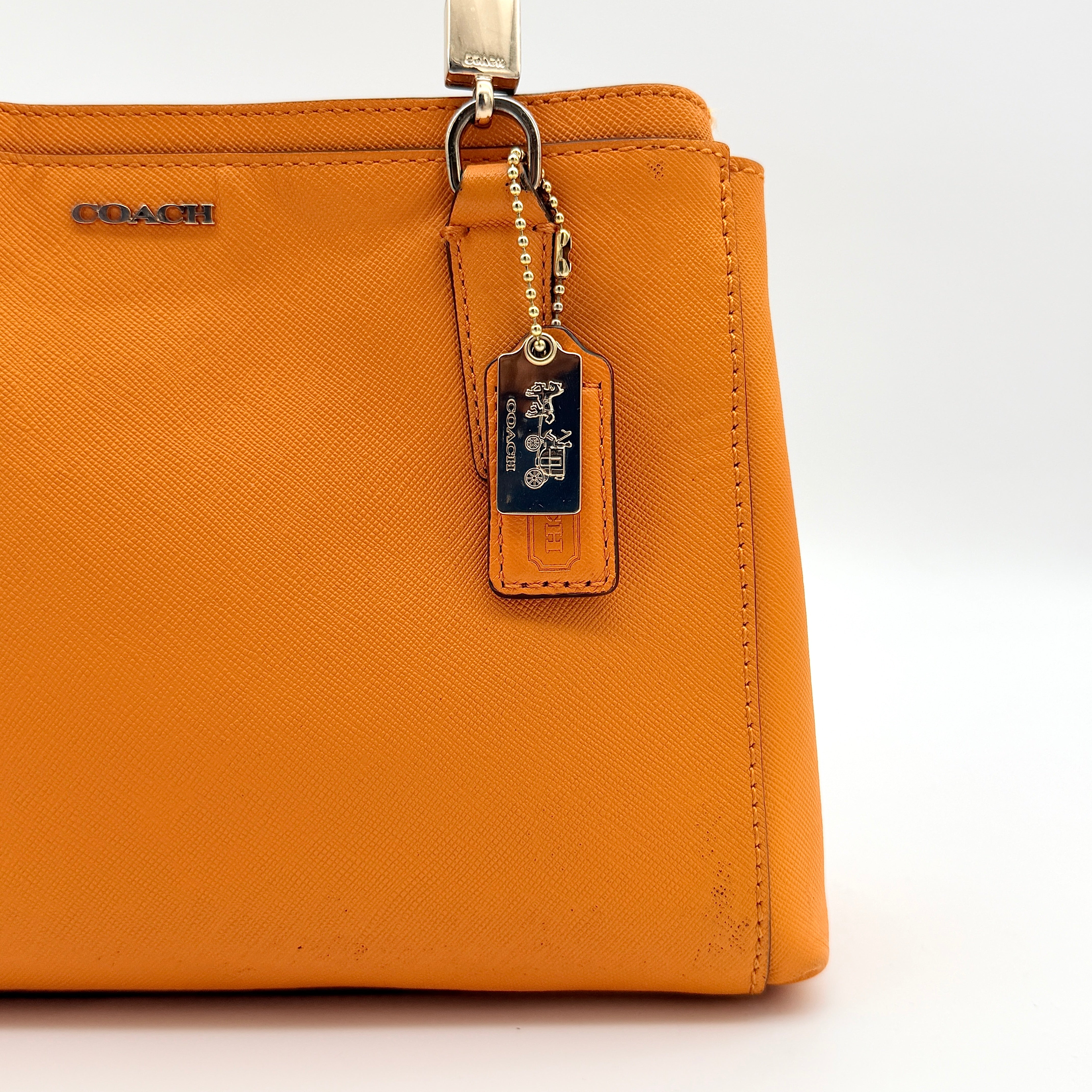 Coach Christie Carryall handbag in orange leather with gold hardware and structured handles, photographed on a white background.
