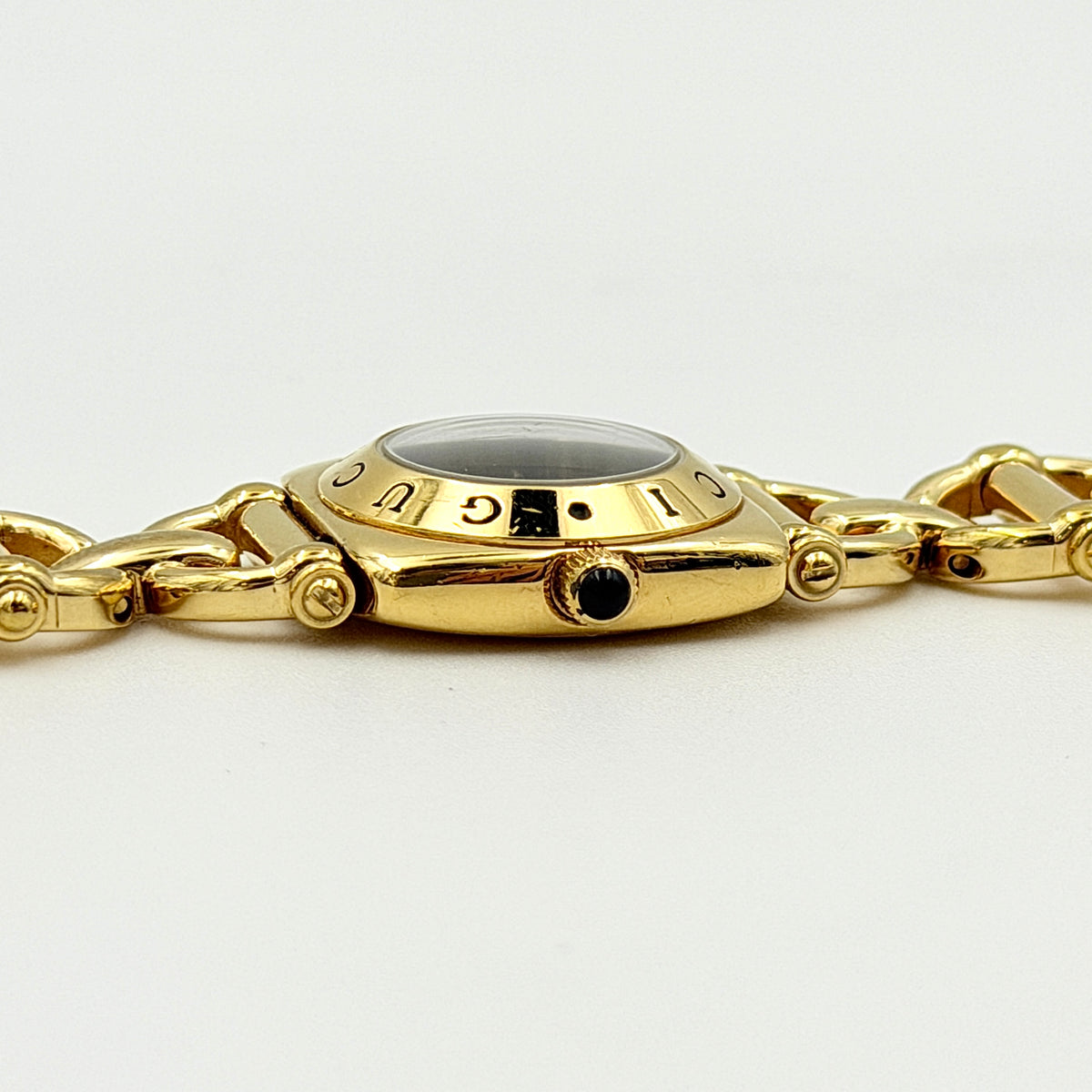 Gucci 6400L gold-tone bracelet watch with a black dial and distinctive horsebit links, showcased on a clear stand.