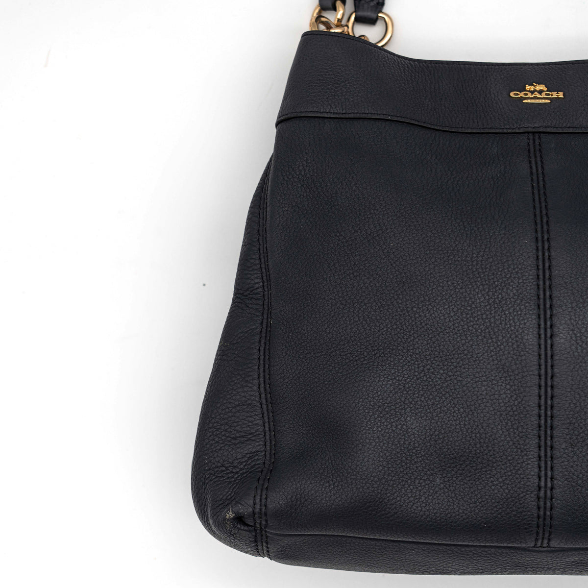 Coach Lexy Shoulder Bag in black pebbled leather with gold-tone hardware and double handles, styled against a white background.
