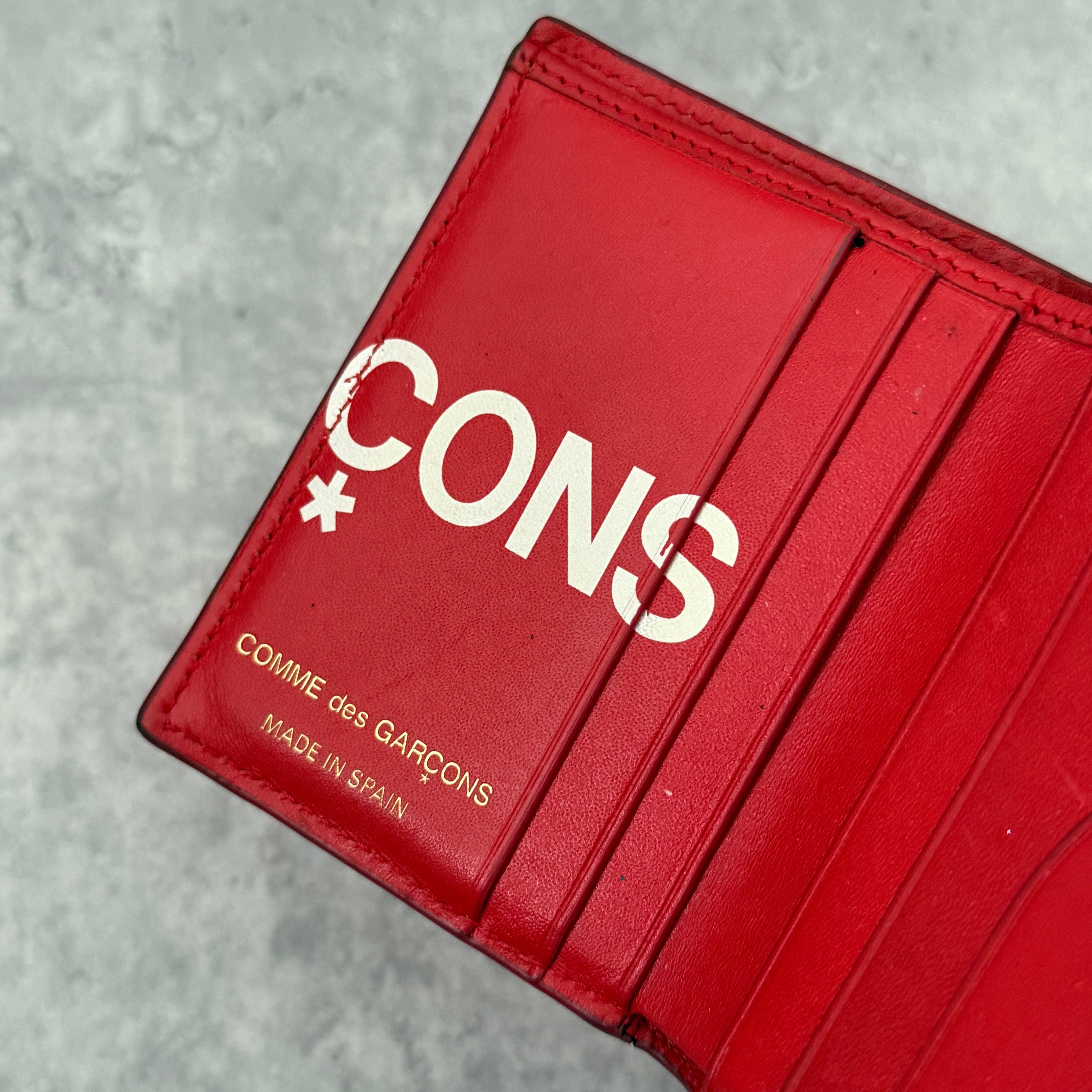 COMME des GARÇONS Huge Logo Red Leather Wallet with oversized white print and multiple card slots in a bi-fold design.