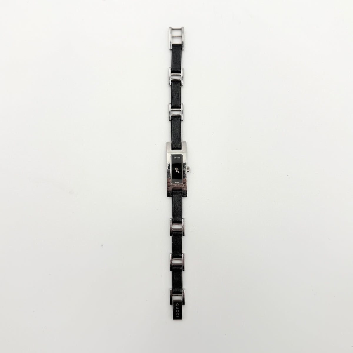 Gucci 3900L black dial watch with silver-tone rectangular case and black leather strap displayed on a stand