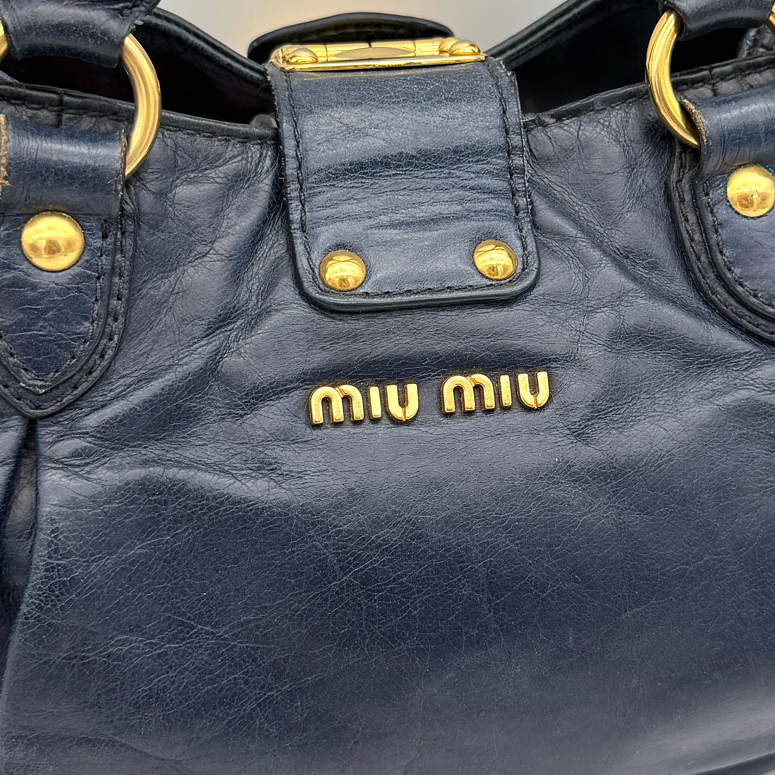 Miu Miu navy blue Vitello Lux Bow Satchel with gold-tone hardware, detachable strap, and dust bag.