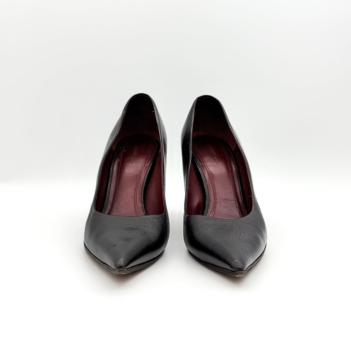 A pair of black leather Celine stiletto heels with pointed toes and burgundy insoles, shown in a softly lit studio setting.