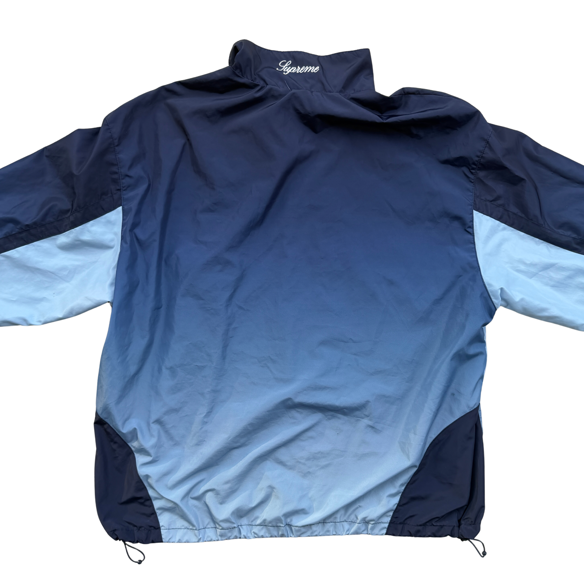 Supreme x Umbro blue gradient track jacket with white Supreme Champions lettering and crest, shown zipped with elastic cuffs and hem.