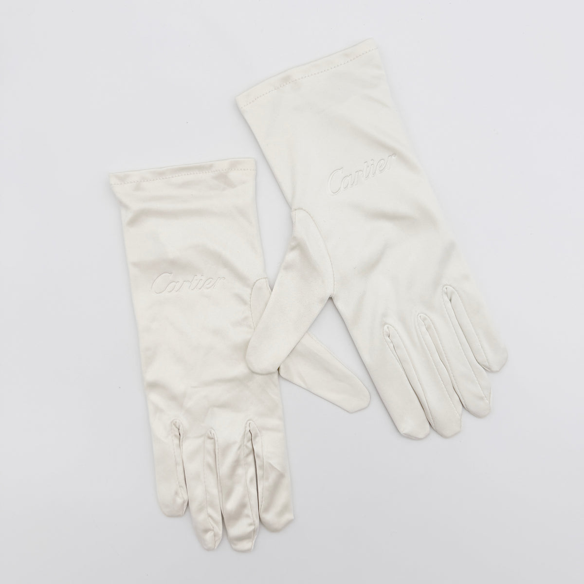 Pair of Cartier ivory gloves with signature script logo embroidery displayed on a flat white background.