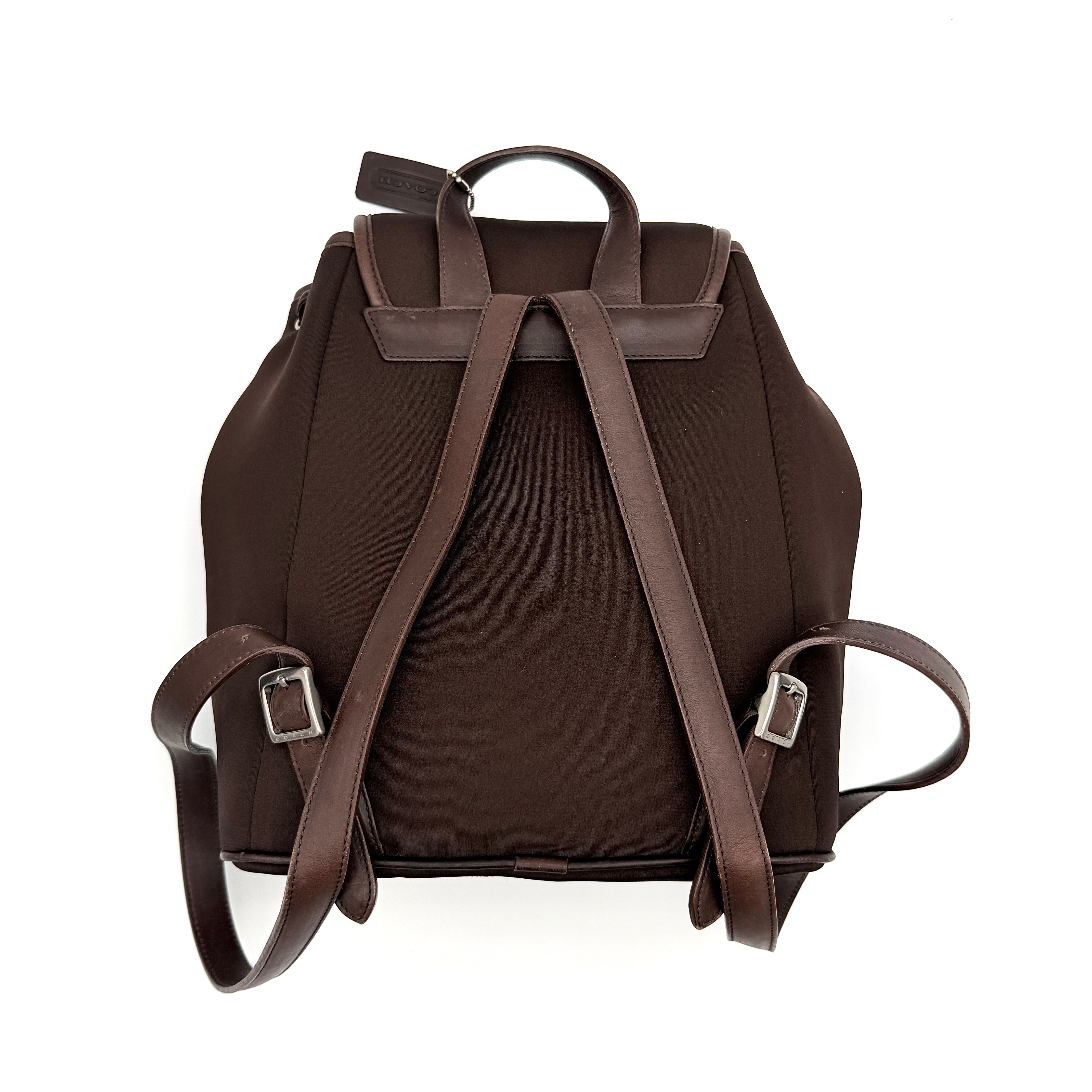 Coach brown neoprene drawstring backpack with leather trim, silver-tone hardware, and adjustable straps shown against a white background.