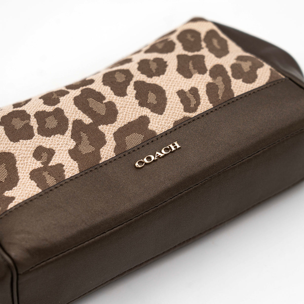 Coach cosmetic pouch in brown and beige leopard print canvas with chocolate leather trim and gold hardware, shown with wrist strap.