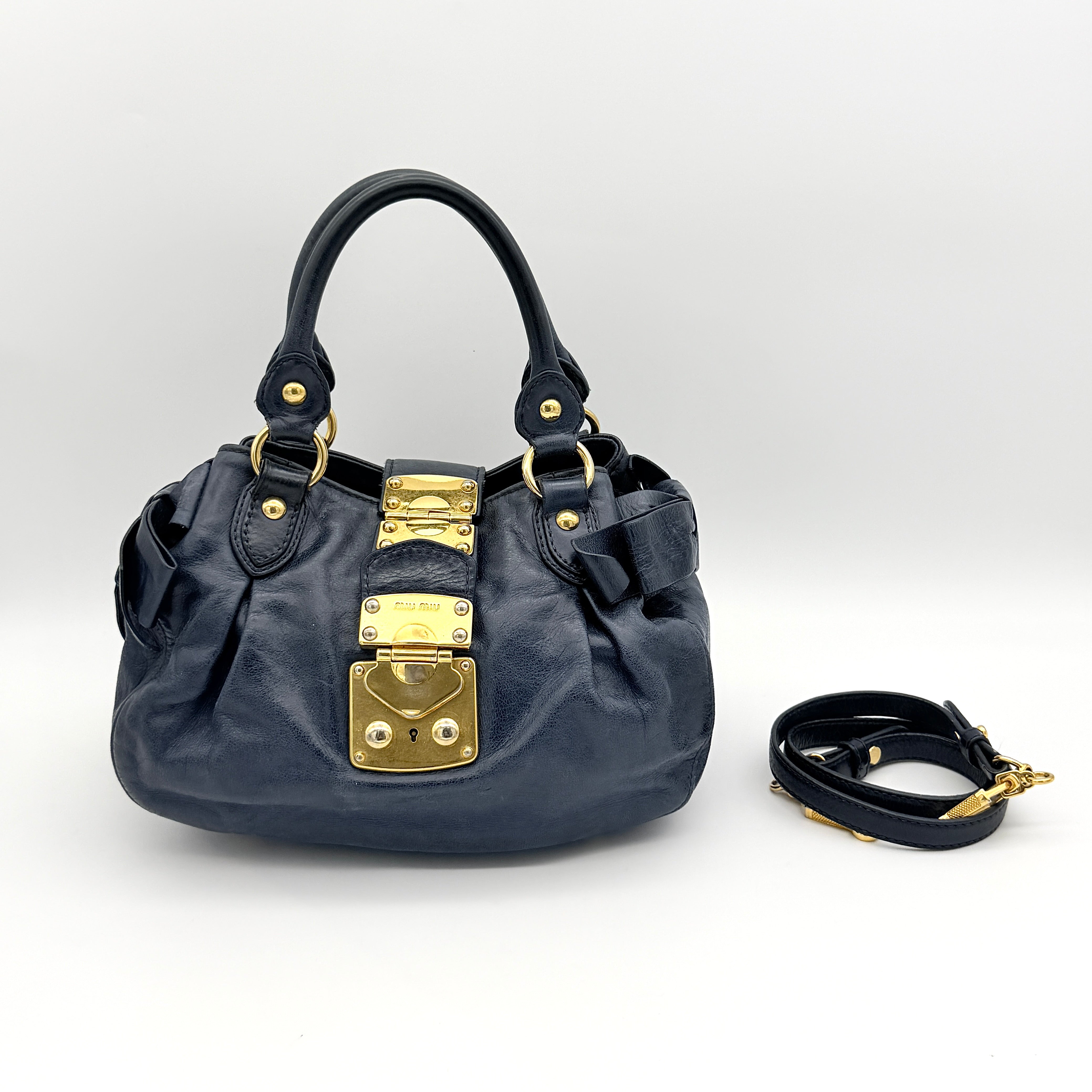 Miu Miu navy blue Vitello Lux Bow Satchel with gold-tone hardware, detachable strap, and dust bag.