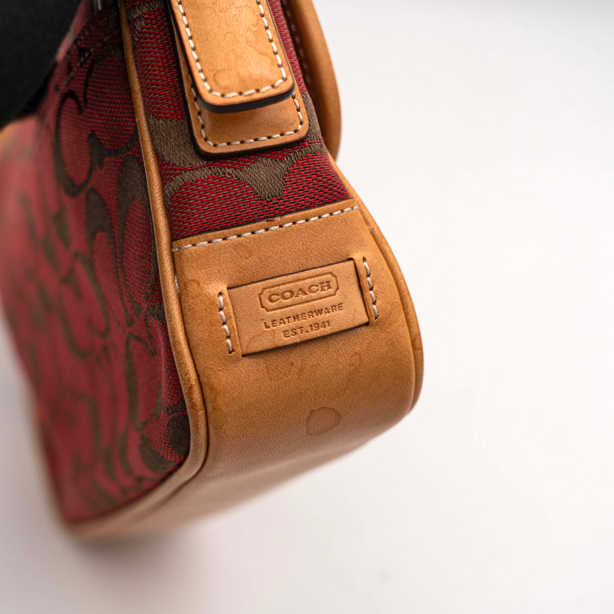 Coach Signature Soho Buckle Baguette in red and tan canvas with leather trim and a silver buckle, shown on a white background.
