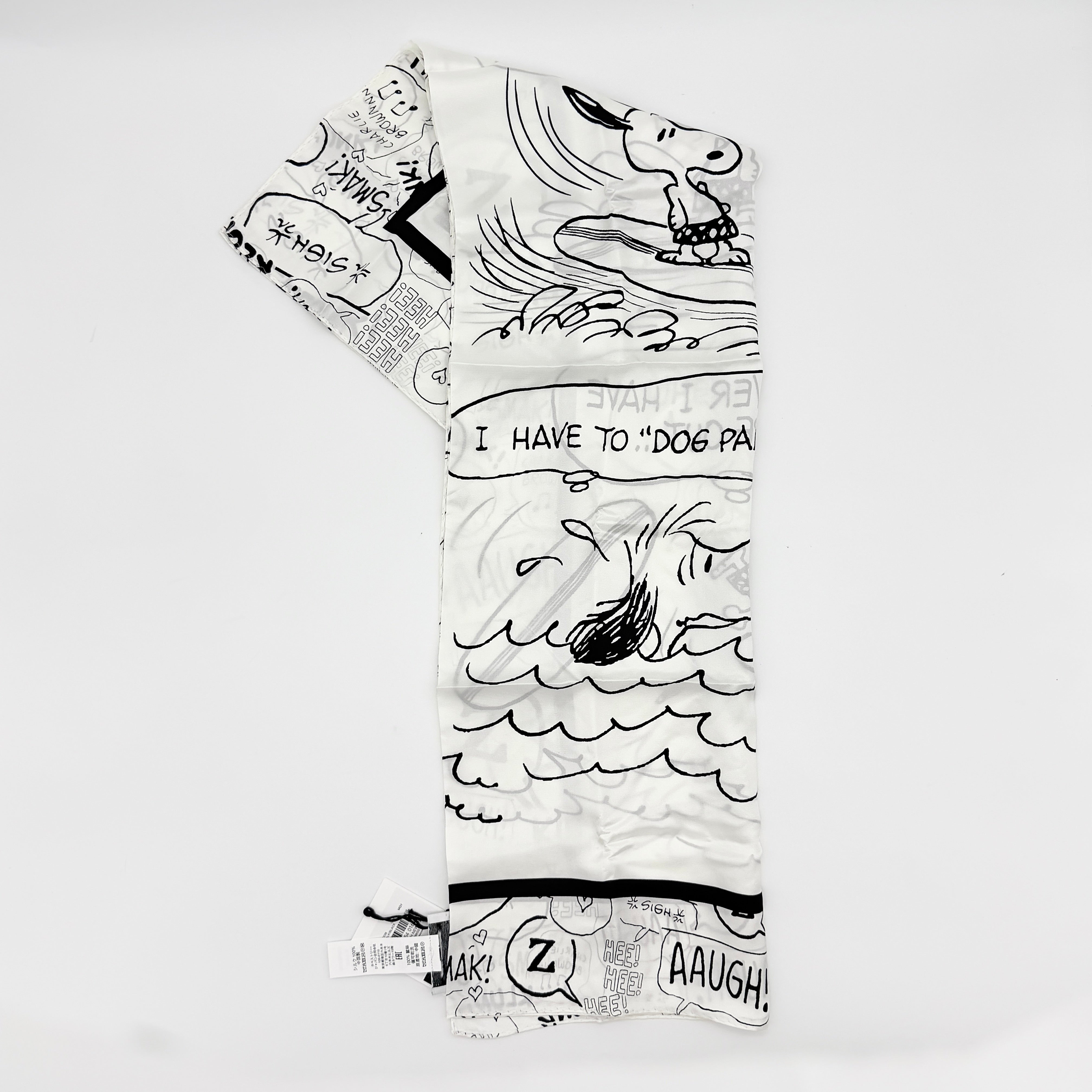 Coach x Peanuts black and white silk scarf featuring a Snoopy surfing comic print, shown with Coach packaging and tags.