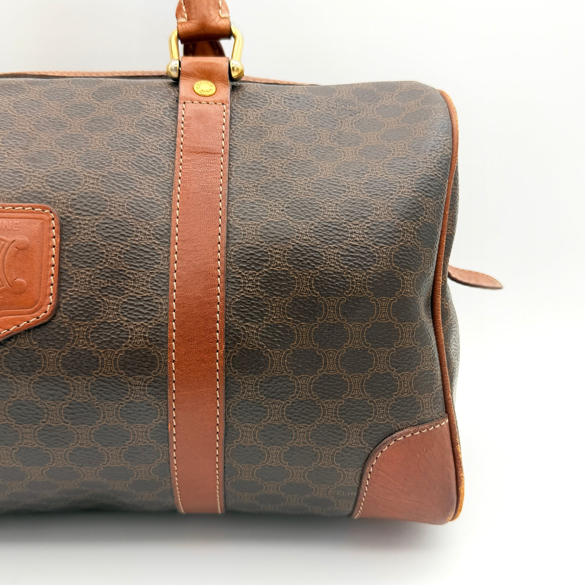 Celine Macadam Triomphe Boston Bag in brown coated canvas with tan leather and gold-tone hardware, shown against a white background.