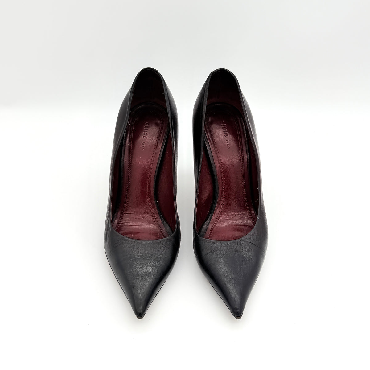 A pair of black leather Celine stiletto heels with pointed toes and burgundy insoles, shown in a softly lit studio setting.