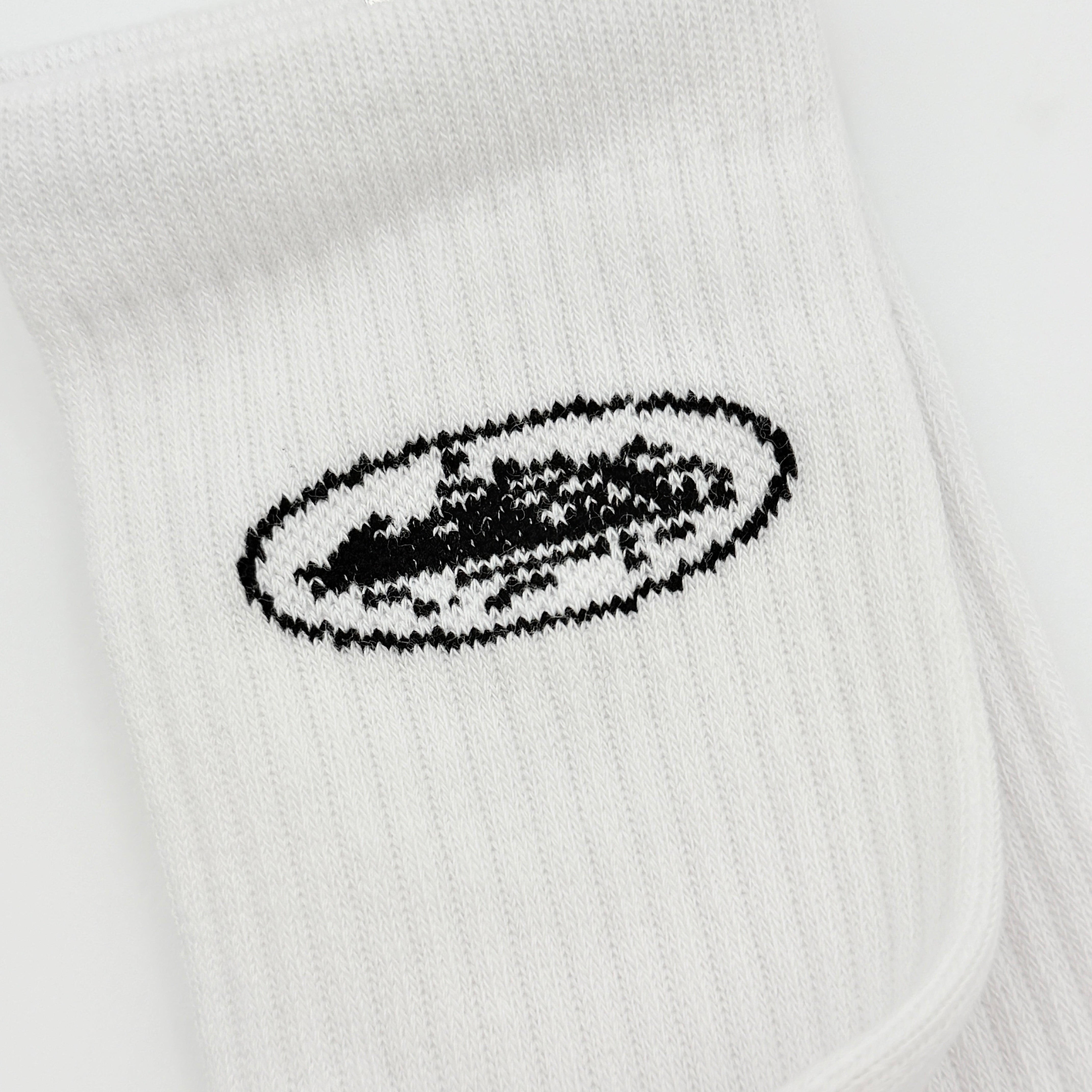 A pair of Corteiz Alcatraz white socks with black logo on the ankle and statement text on the sole.