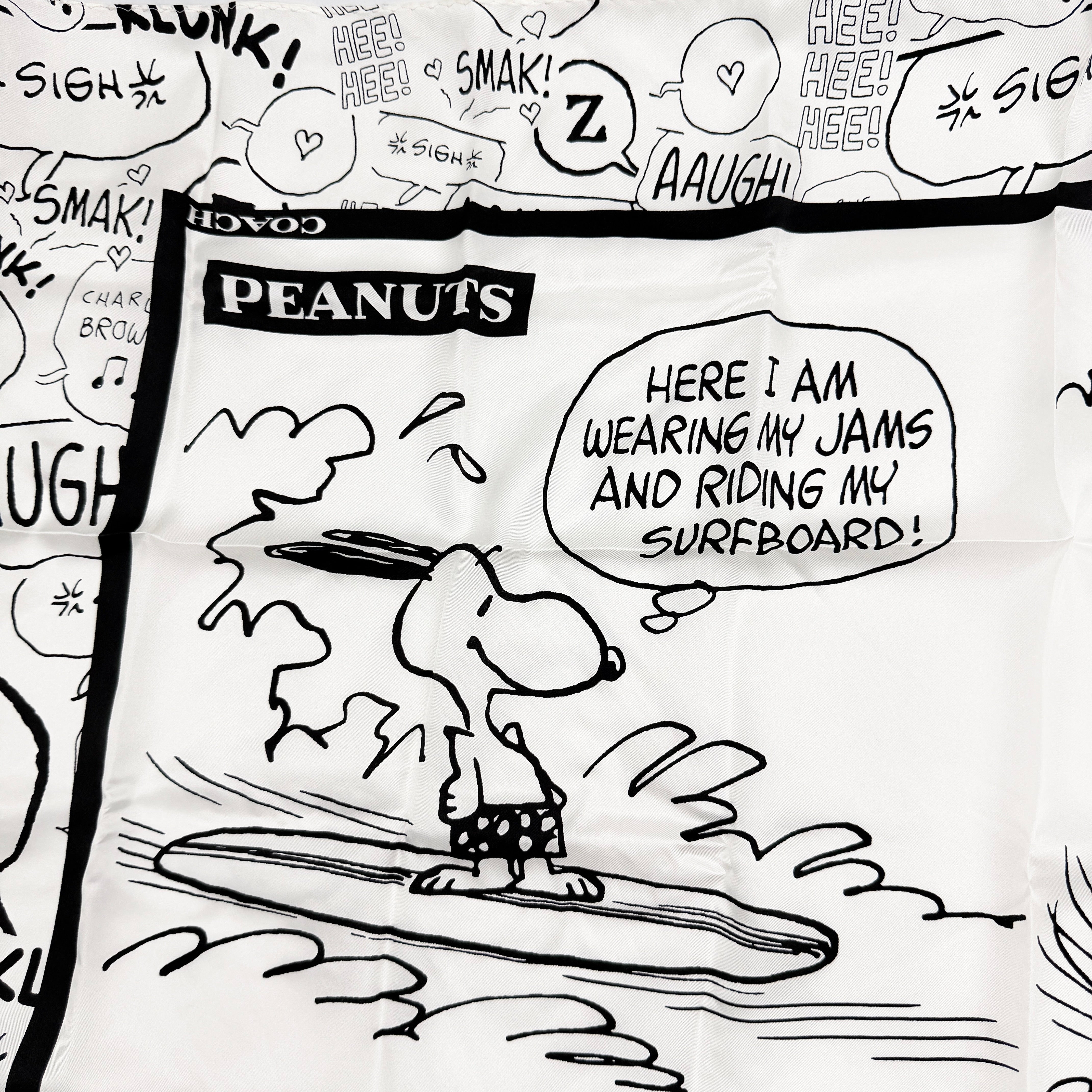 Coach x Peanuts black and white silk scarf featuring a Snoopy surfing comic print, shown with Coach packaging and tags.