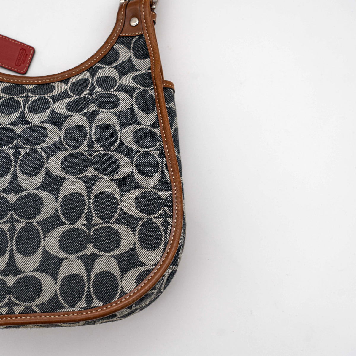Coach signature denim hobo crossbody bag with red and blue stripe, brown leather trim, and an adjustable strap.