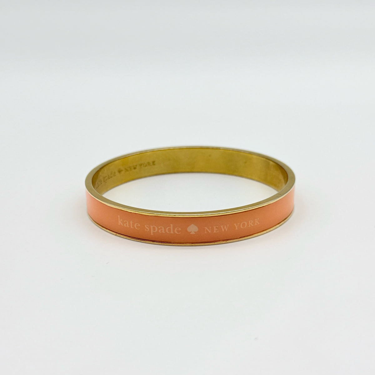 Kate Spade New York enamel bangle in orange with gold-tone interior and logo detailing, photographed on a white background.