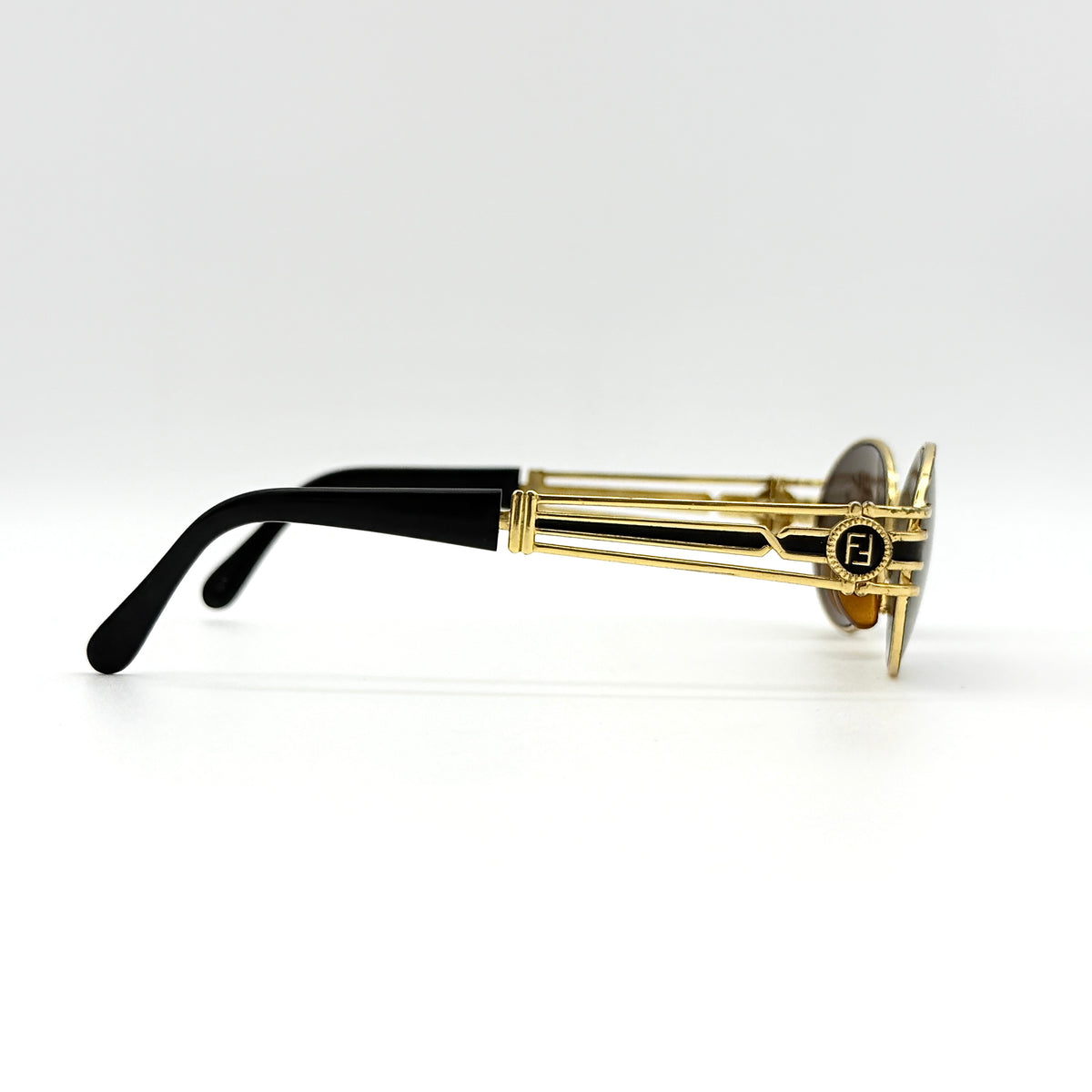 Fendi FF SL7031 oval sunglasses with gold-tone frame, brown lenses, and black arms, shown at an angled side view.