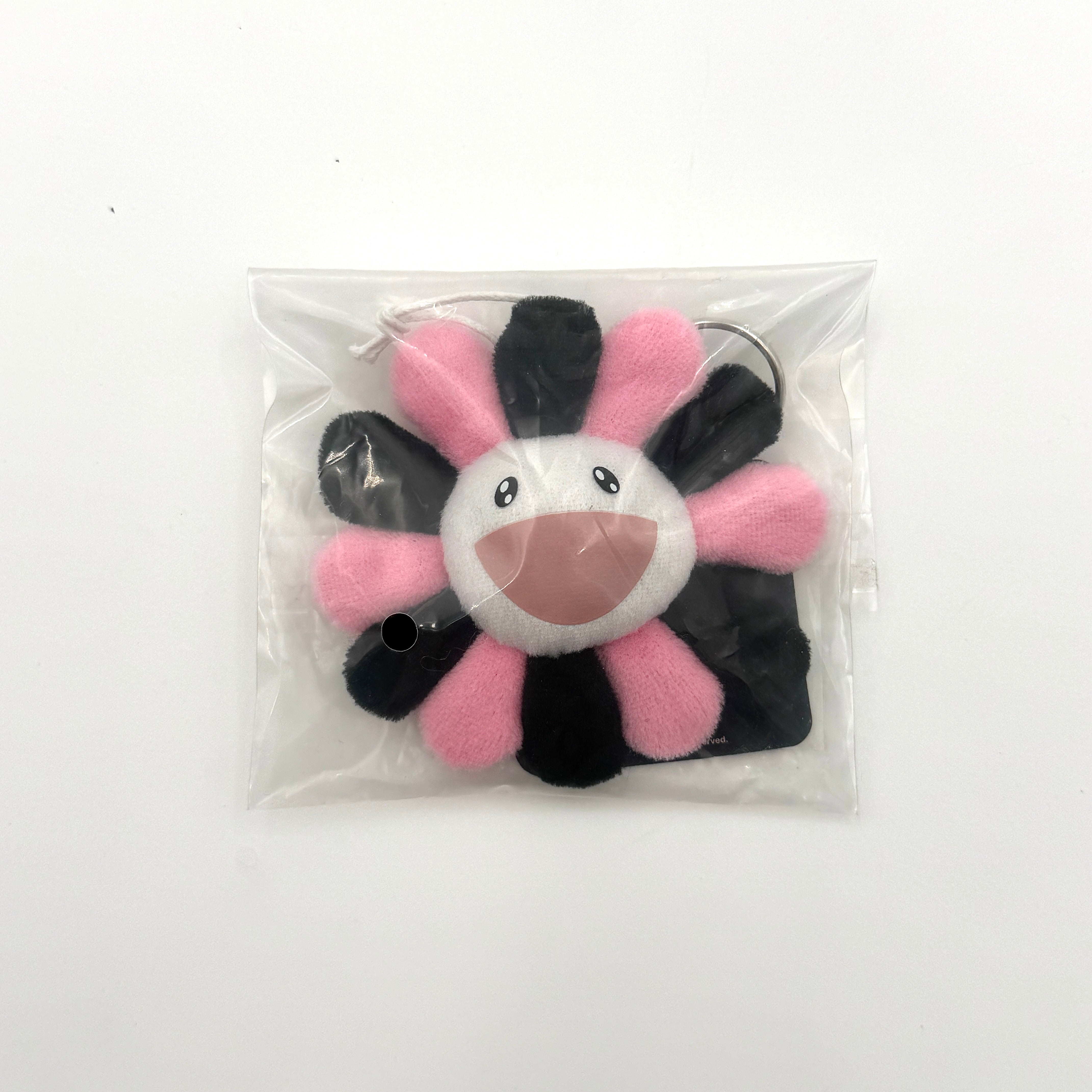 Takashi Murakami x BLACKPINK plush flower keychain in black and pink with smiling face and branded tag.
