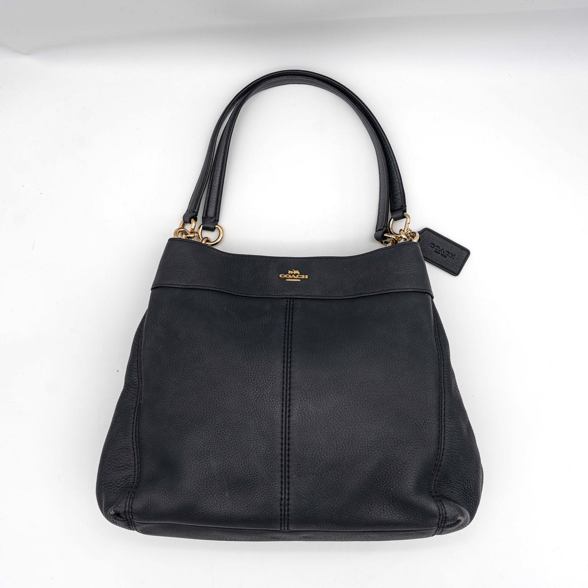 Coach Lexy Shoulder Bag in black pebbled leather with gold-tone hardware and double handles, styled against a white background.