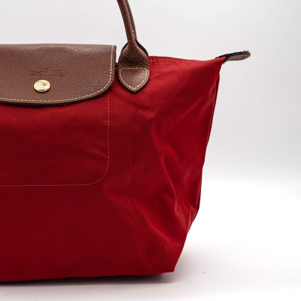 Longchamp Le Pliage handbag in red nylon with brown leather handles and gold-tone accents, photographed on a white background.