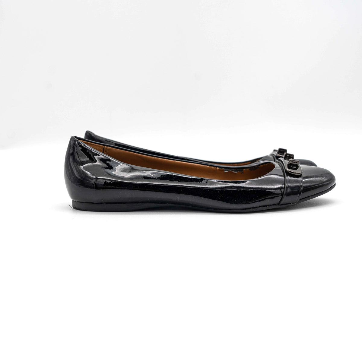 Coach Oswald Turnlock black patent leather ballet flats with dark metal hardware on the toe, photographed on a white background.
