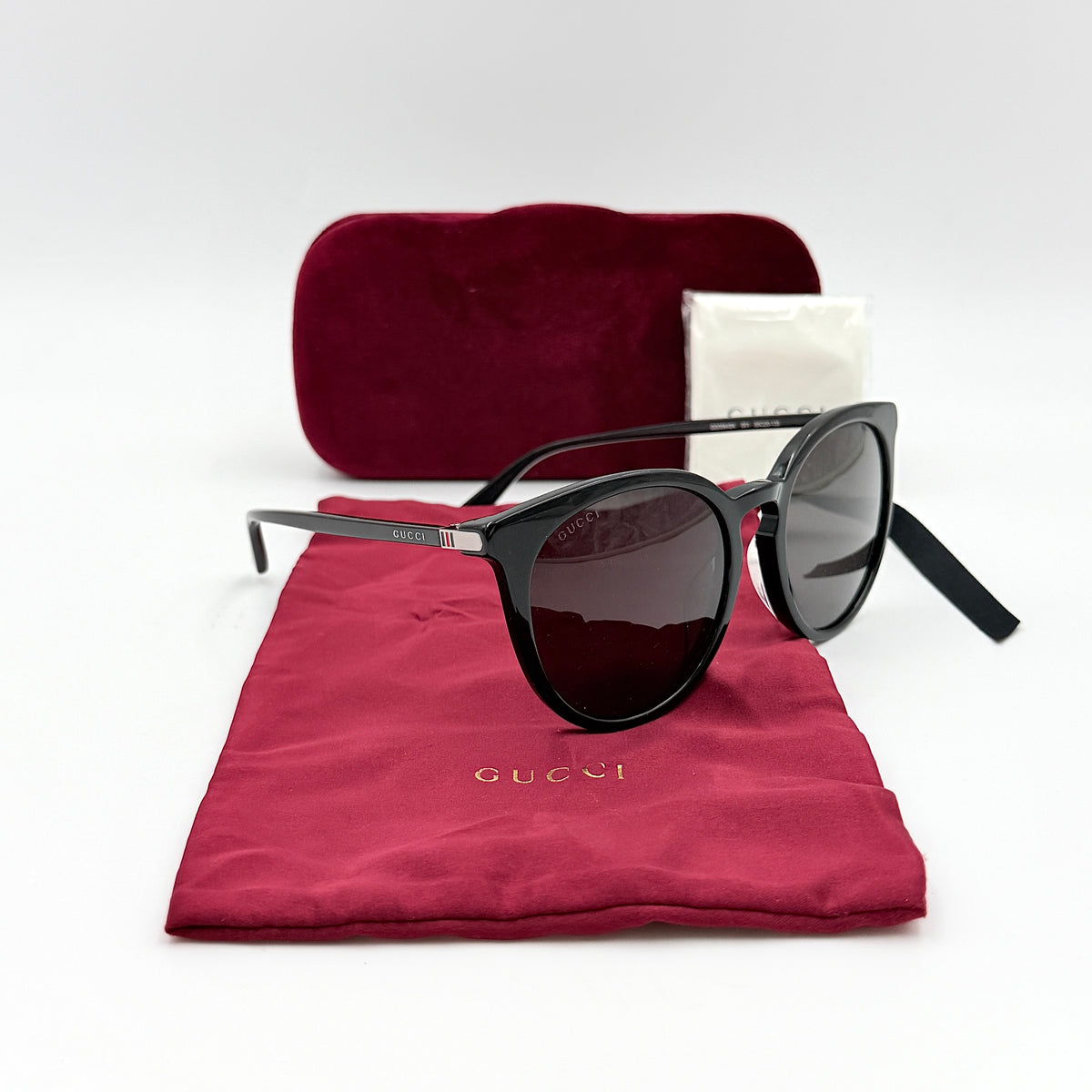 Gucci GG0064SK 001 black round sunglasses with smoky lenses, shown with original burgundy velvet case and pouch.