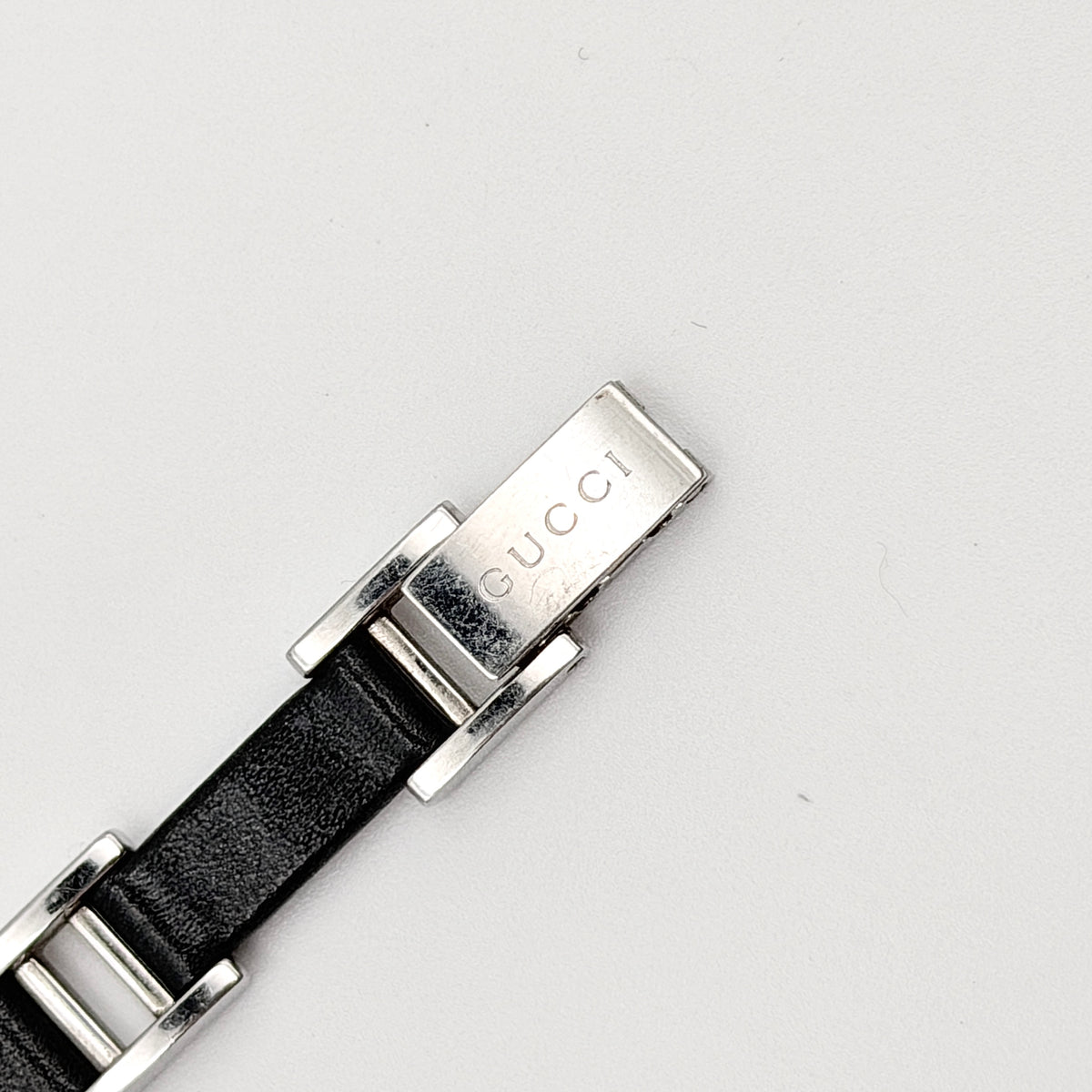 Gucci 3900L black dial watch with silver-tone rectangular case and black leather strap displayed on a stand