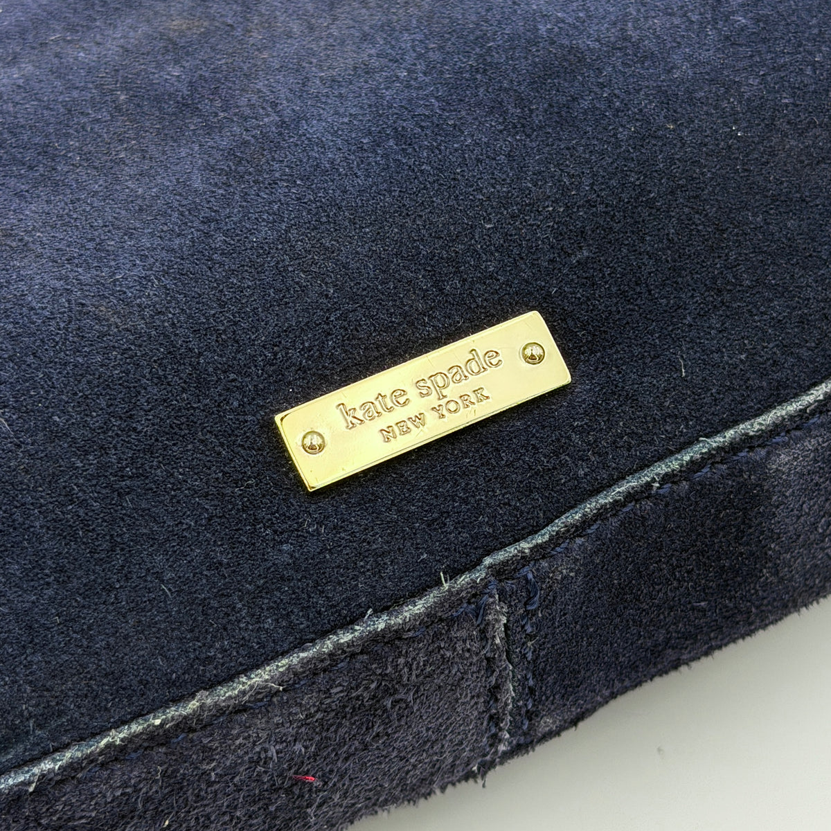 Navy blue suede Kate Spade baguette bag with floral gold hardware and gold-tone shoulder strap.