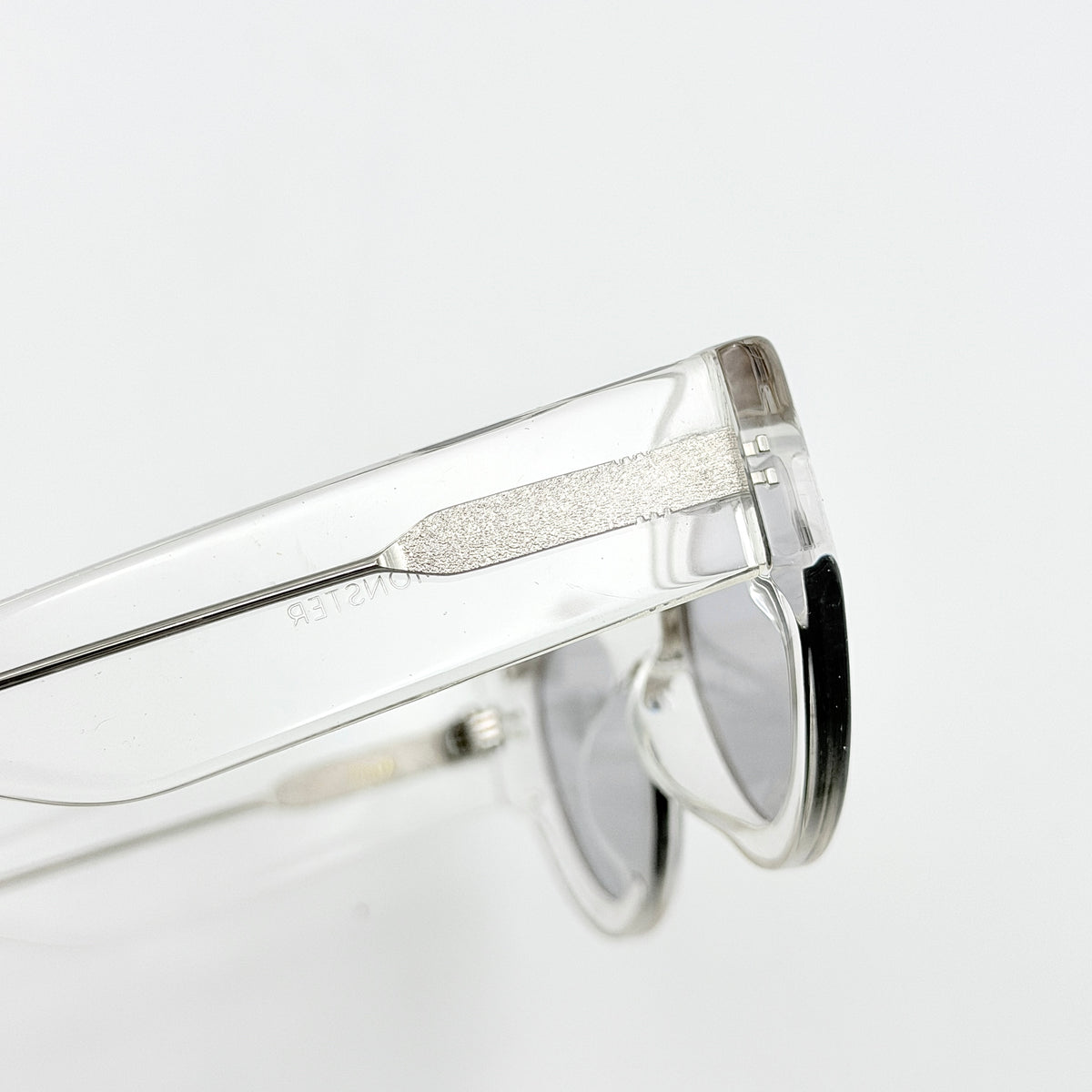 Gentle Monster Tazi transparent sunglasses with grey lenses and clear acetate frame, softly styled alongside the branded case.