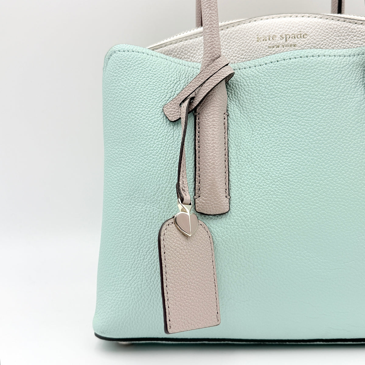 Kate Spade New York Margaux satchel in mint green pebbled leather with taupe handles, shown with its detachable strap and a clear pouch.