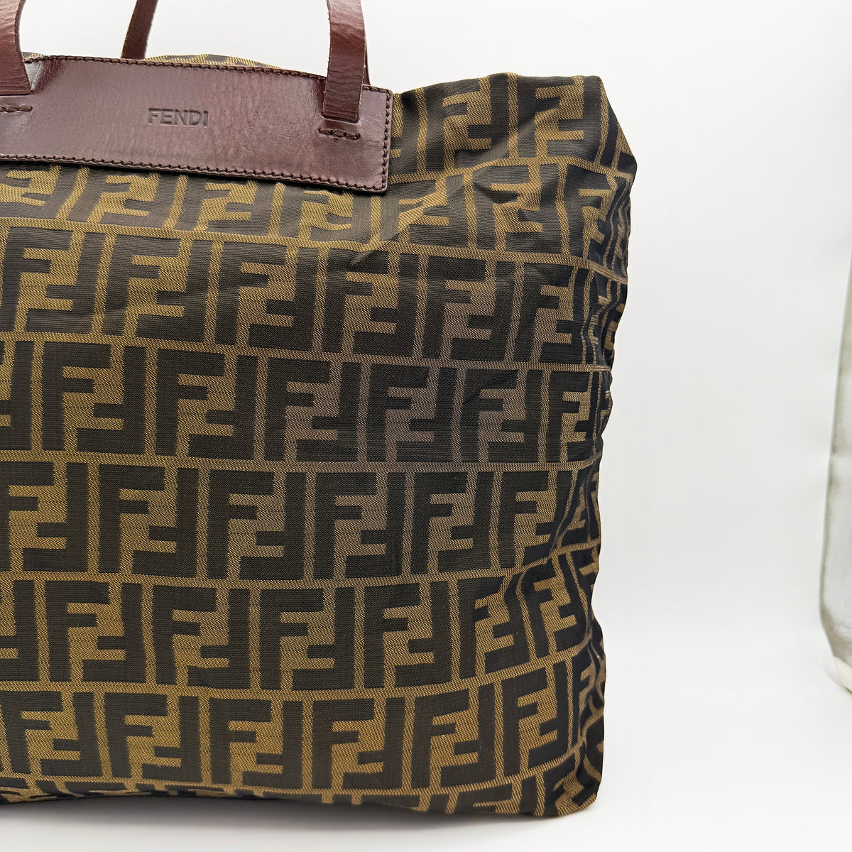 Fendi FF Zucca foldable tote bag in brown canvas with leather top handles and all-over monogram, shown standing upright.