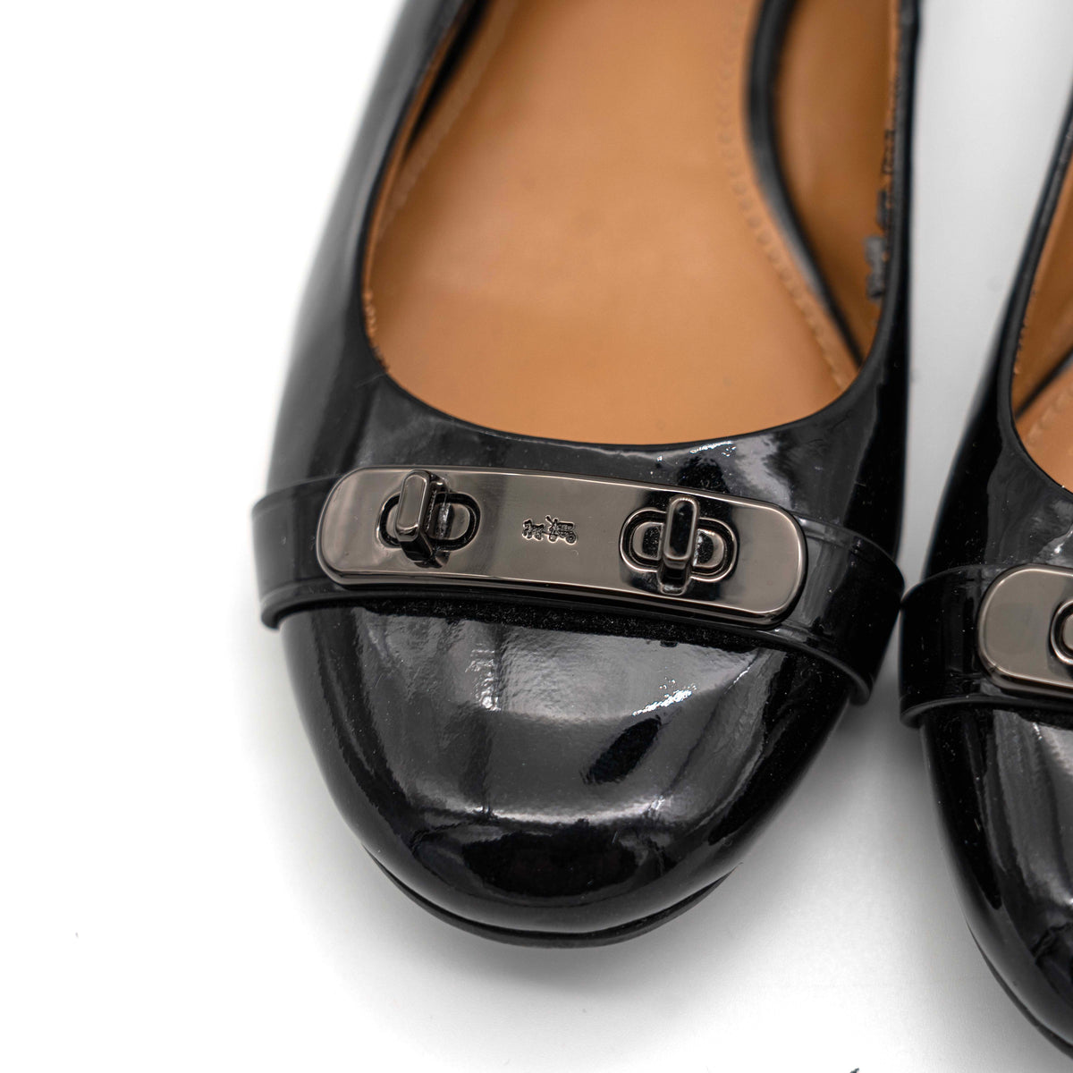 Coach Oswald Turnlock black patent leather ballet flats with dark metal hardware on the toe, photographed on a white background.