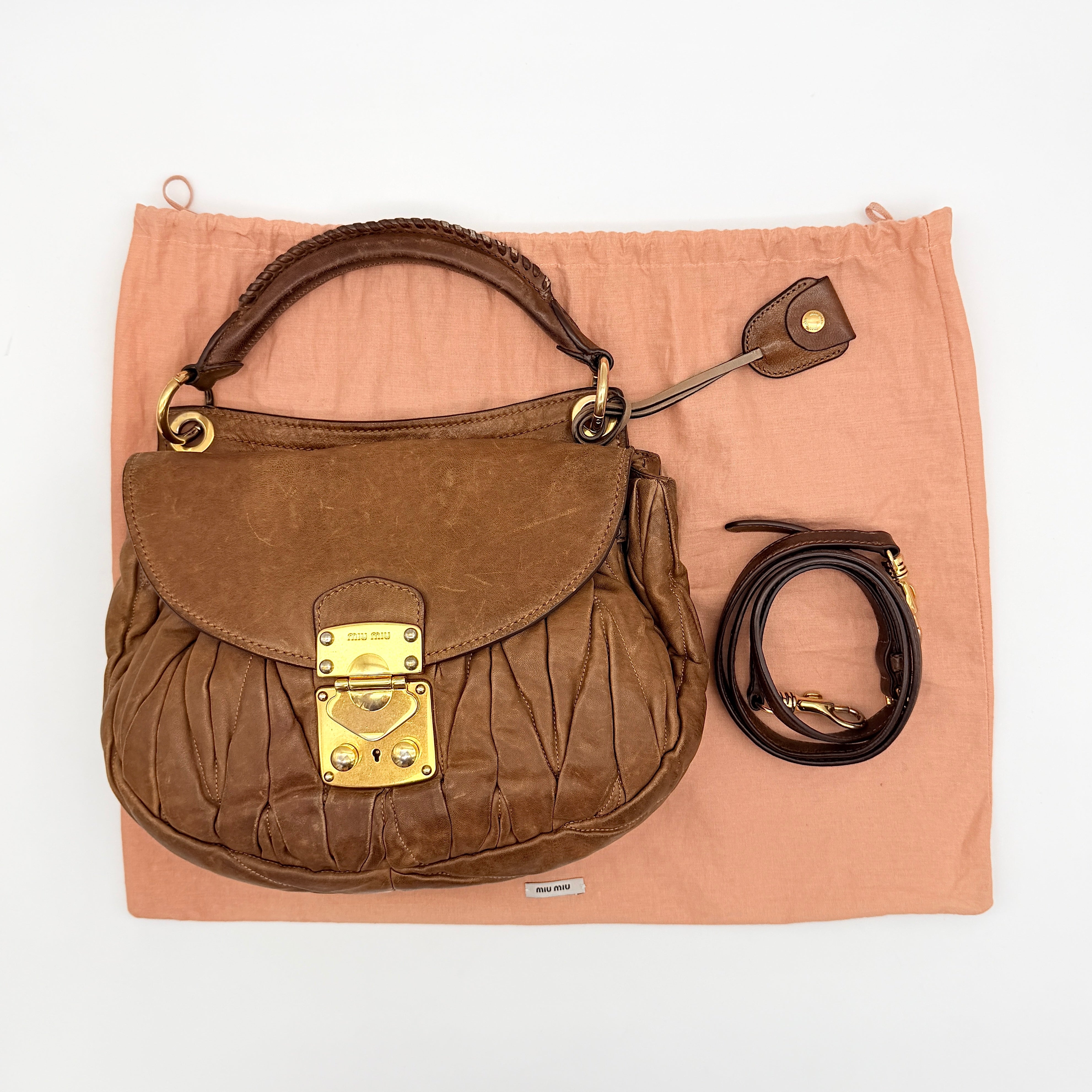 Miu Miu brown Matelasse Coffer Hobo bag with gold hardware, detachable strap, and dust bag displayed on a flat surface.