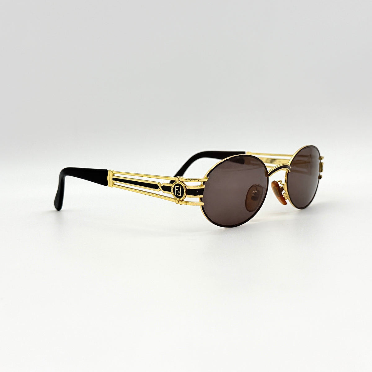 Fendi FF SL7031 oval sunglasses with gold-tone frame, brown lenses, and black arms, shown at an angled side view.