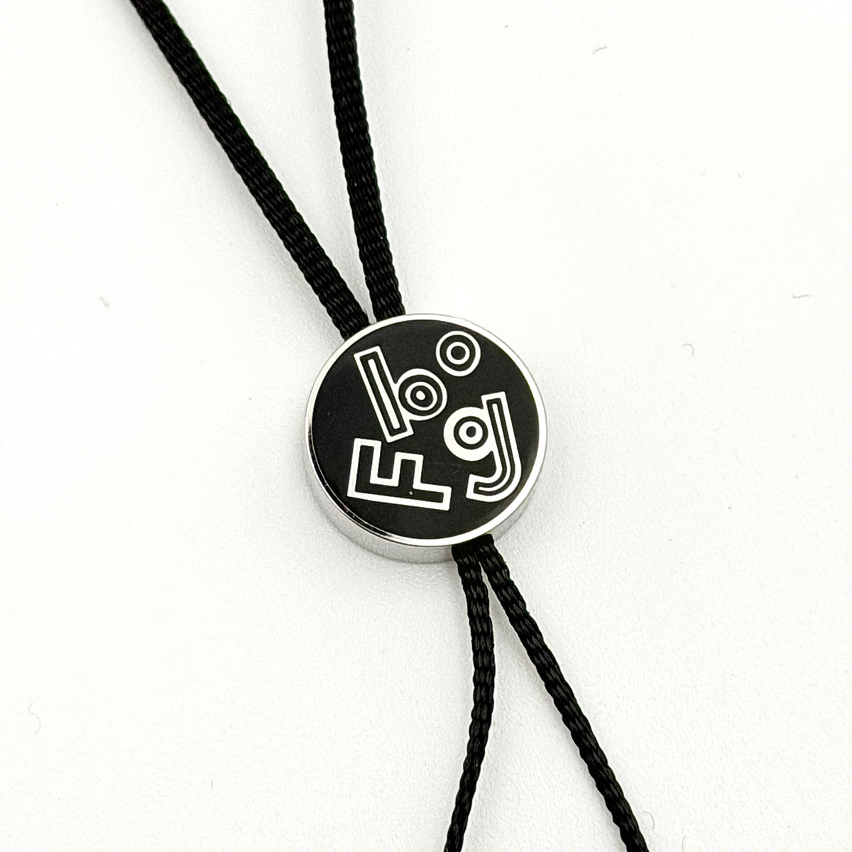 Hermès black cord cell phone charm strap with round silver-tone graphic accent, shown against a white background.