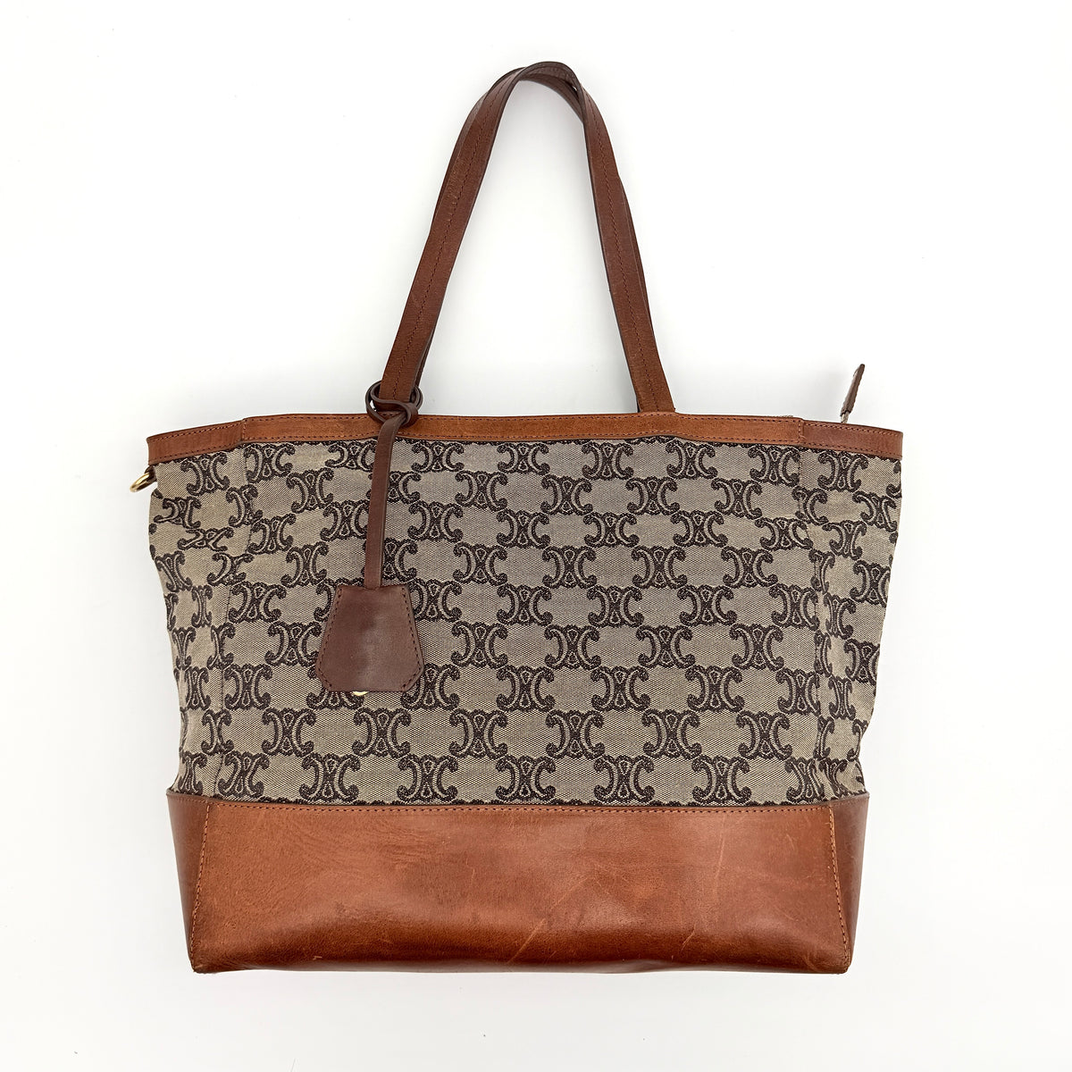 Celine Triomphe Macadam Canvas Tote Bag in beige and brown with leather trim and top handles, styled against a white background.