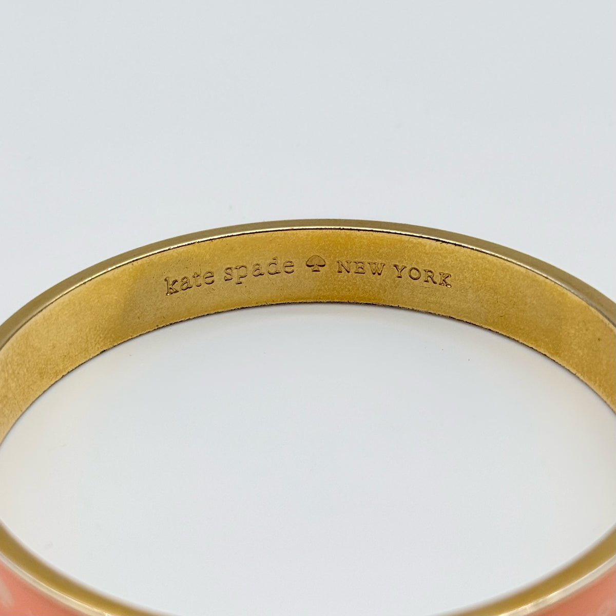 Kate Spade New York enamel bangle in orange with gold-tone interior and logo detailing, photographed on a white background.