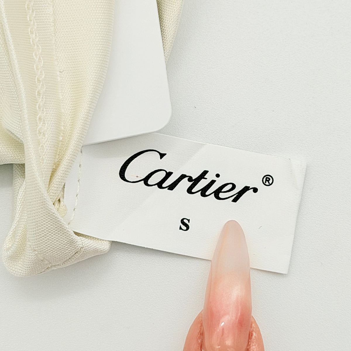 Pair of Cartier ivory gloves with signature script logo embroidery displayed on a flat white background.