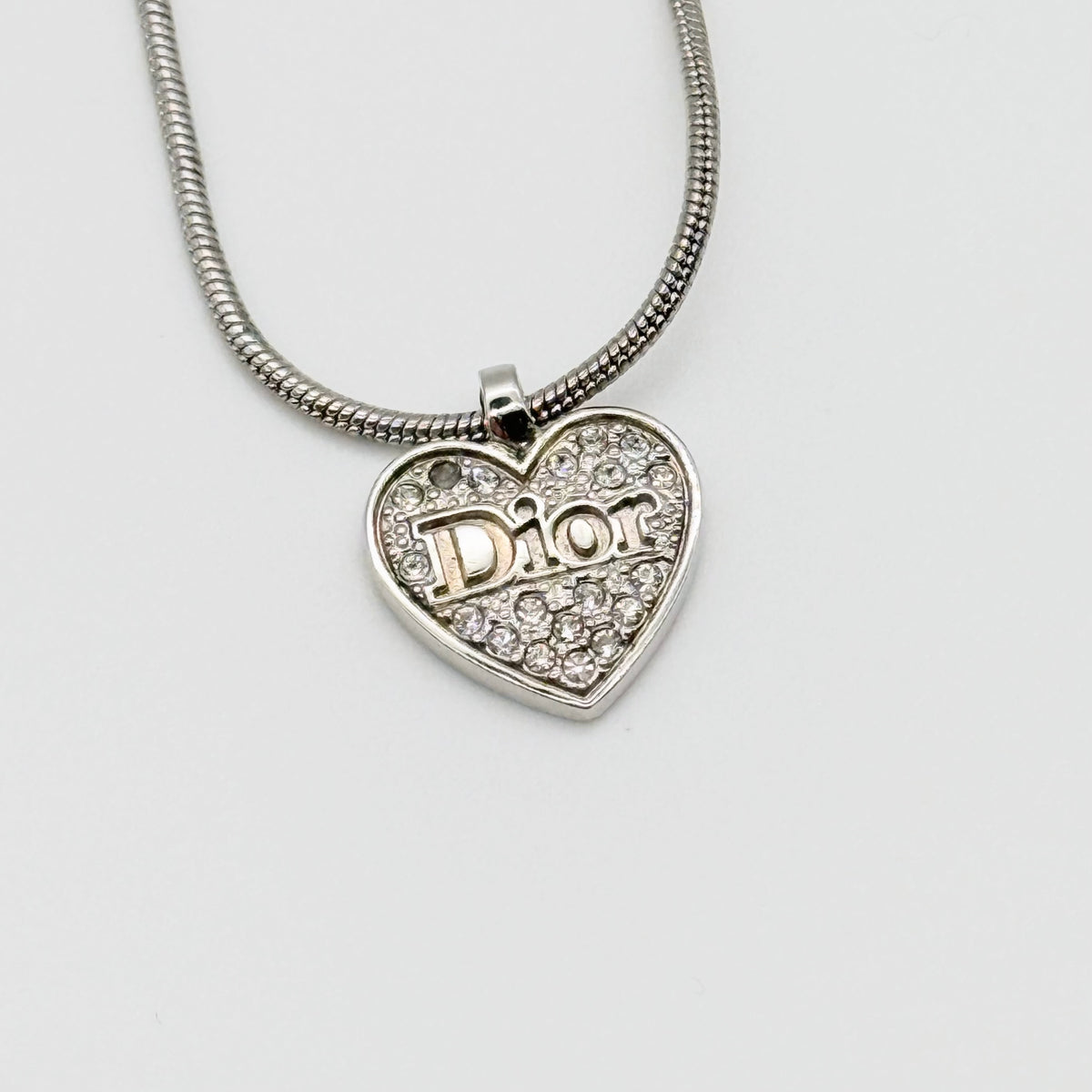 Dior silver necklace with a rhinestone heart pendant and Dior logo, laid flat with CD tag visible.