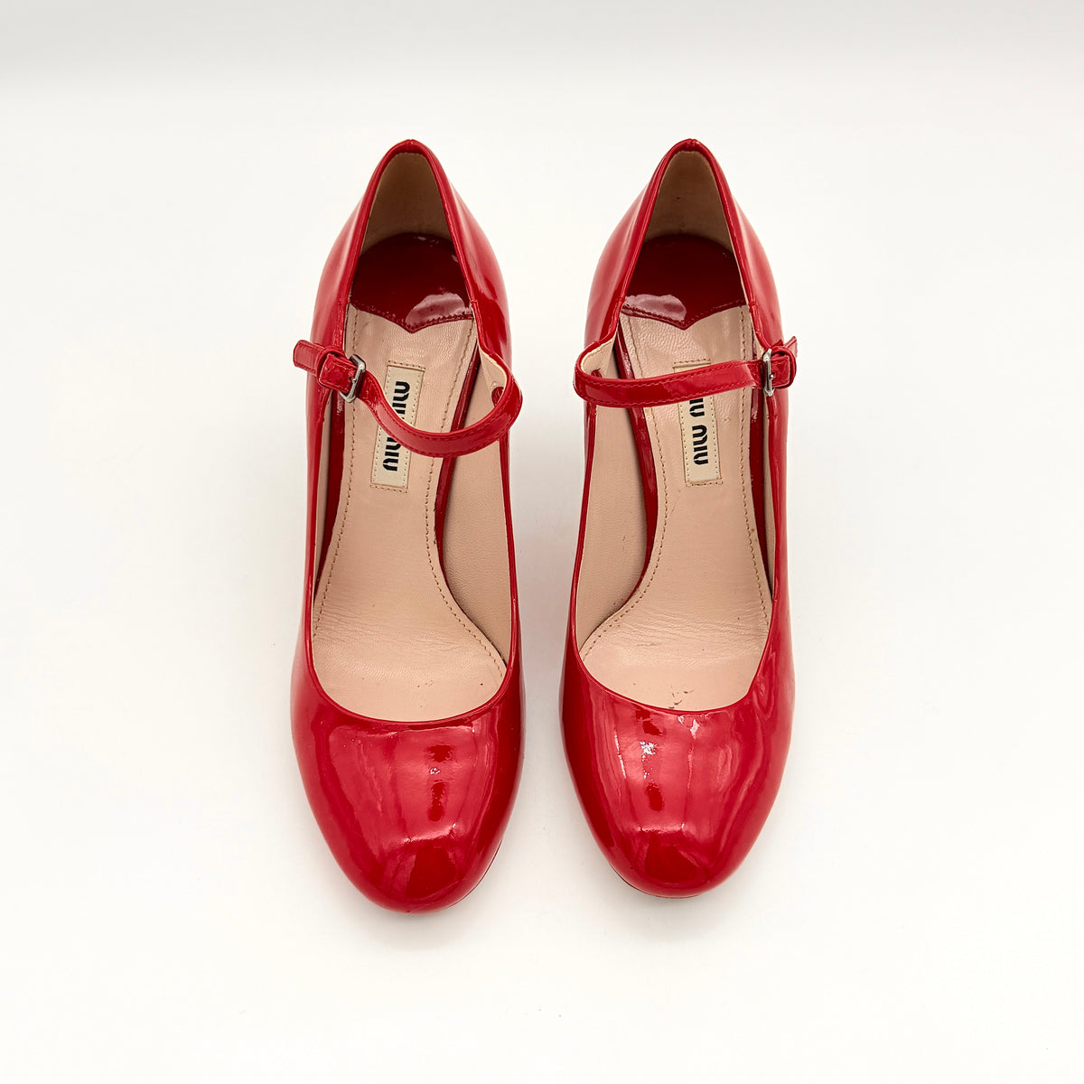 A pair of red patent leather Miu Miu Mary Jane heels with adjustable buckle straps and high heels, displayed against a white background.