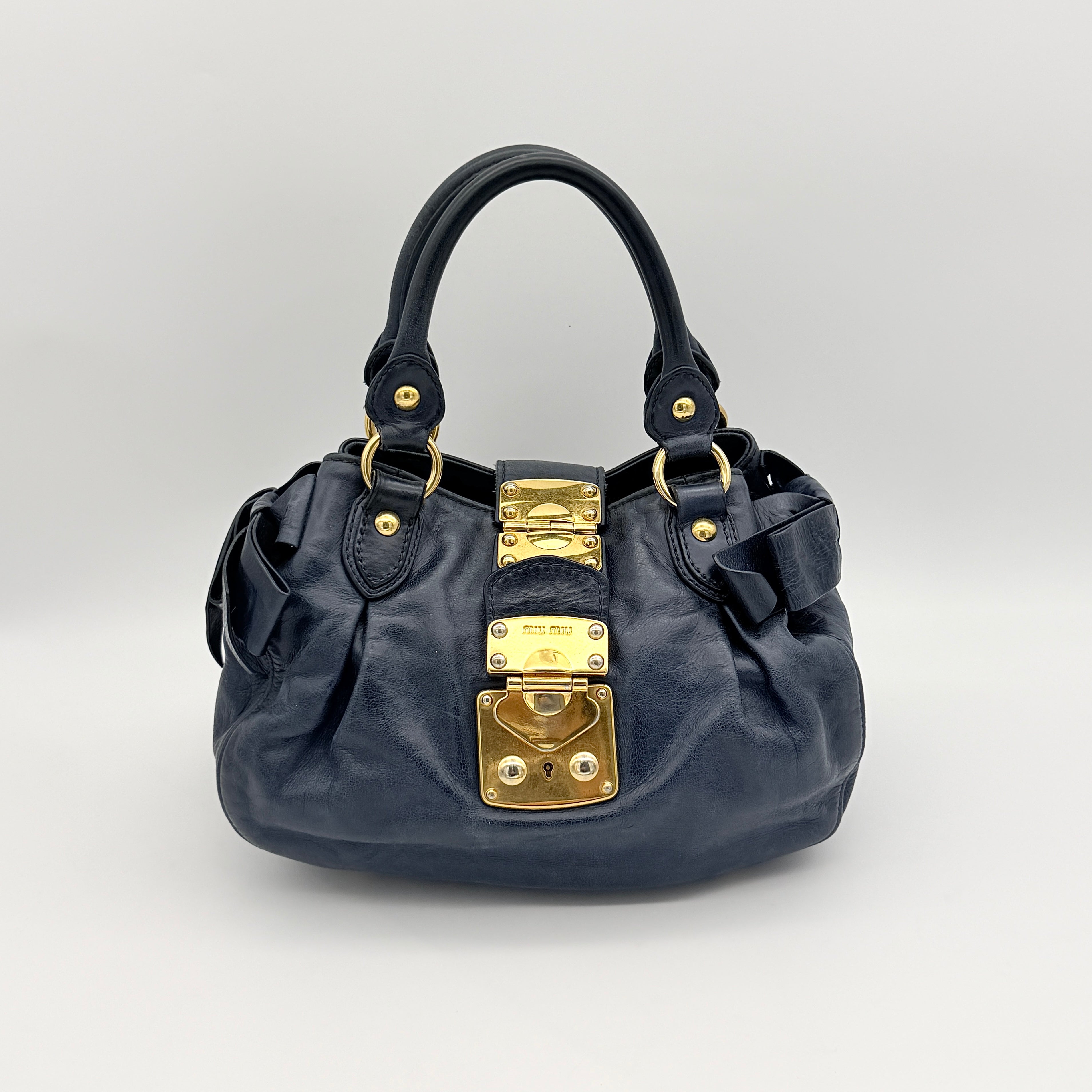 Miu Miu navy blue Vitello Lux Bow Satchel with gold-tone hardware, detachable strap, and dust bag.