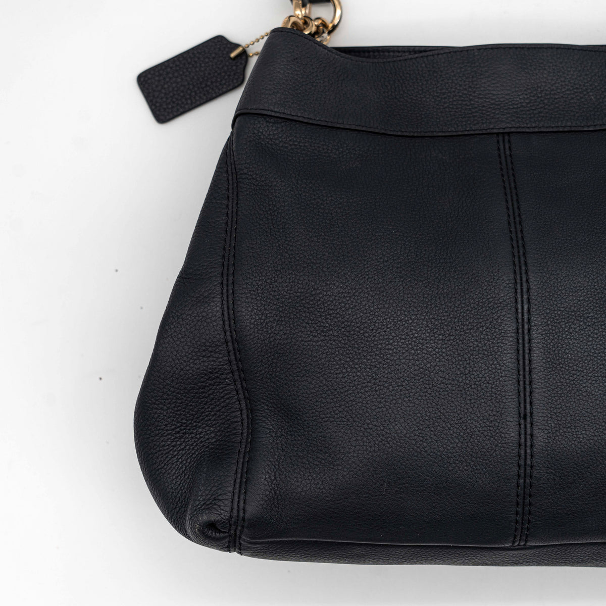 Coach Lexy Shoulder Bag in black pebbled leather with gold-tone hardware and double handles, styled against a white background.