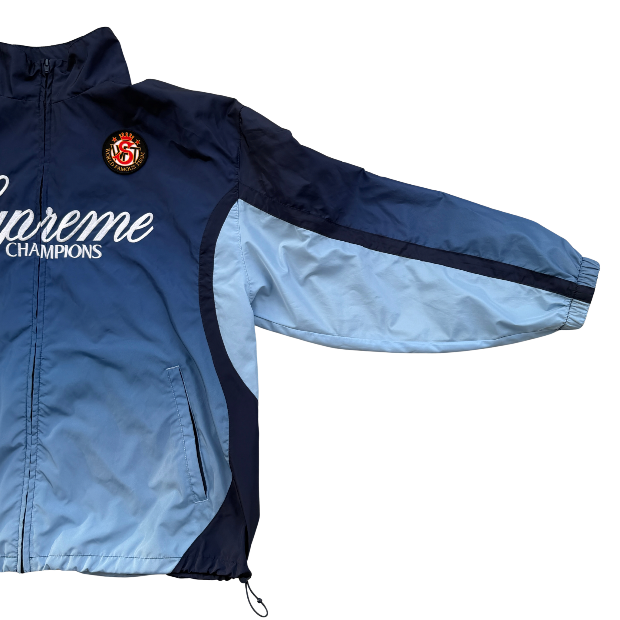 Supreme x Umbro blue gradient track jacket with white Supreme Champions lettering and crest, shown zipped with elastic cuffs and hem.